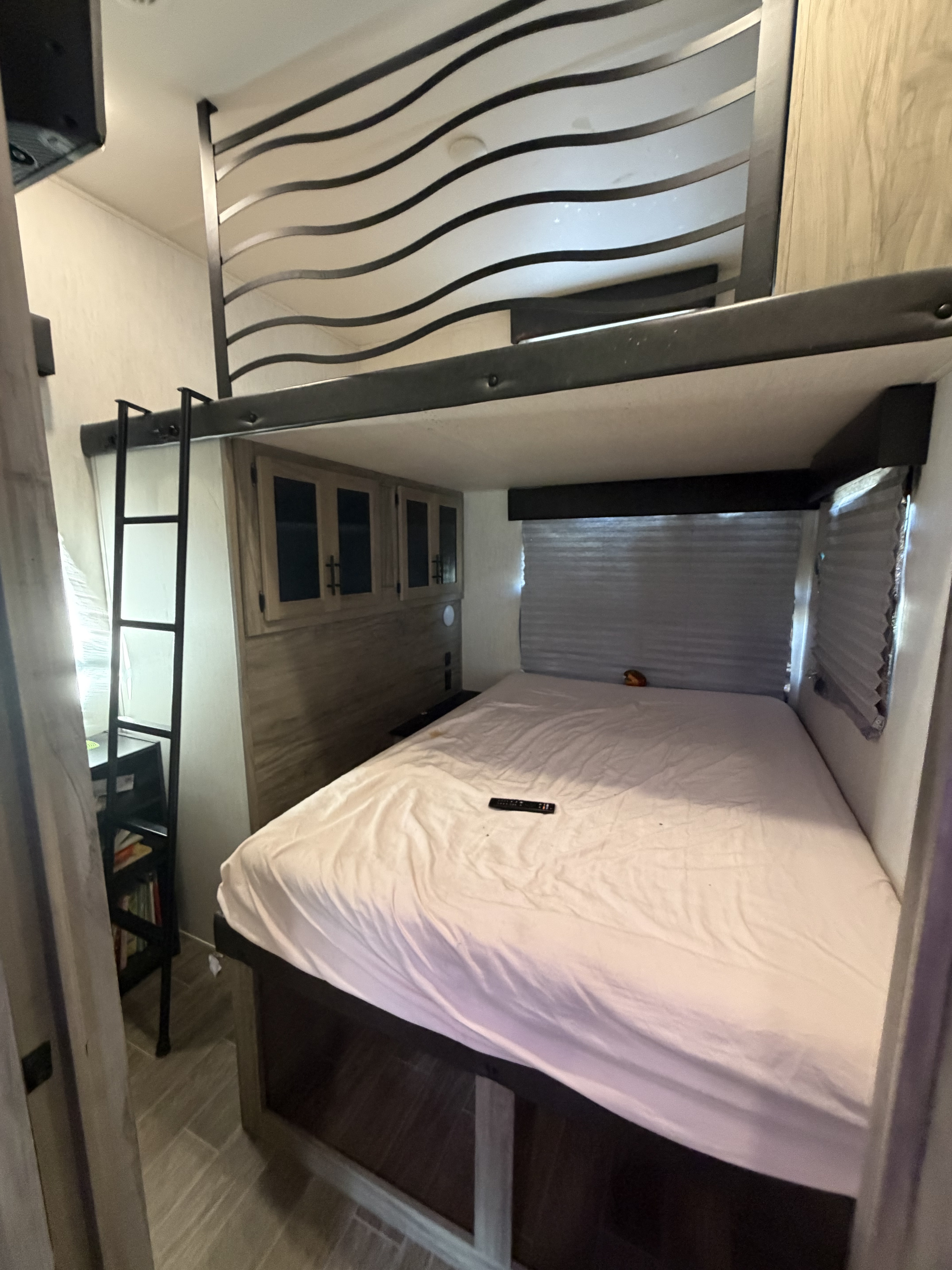 Compact RV rental bedroom with a comfy bed, overhead cabinets, and a loft bunk bed with ladder, optimized for space.. Forest River Artic wolf 2022