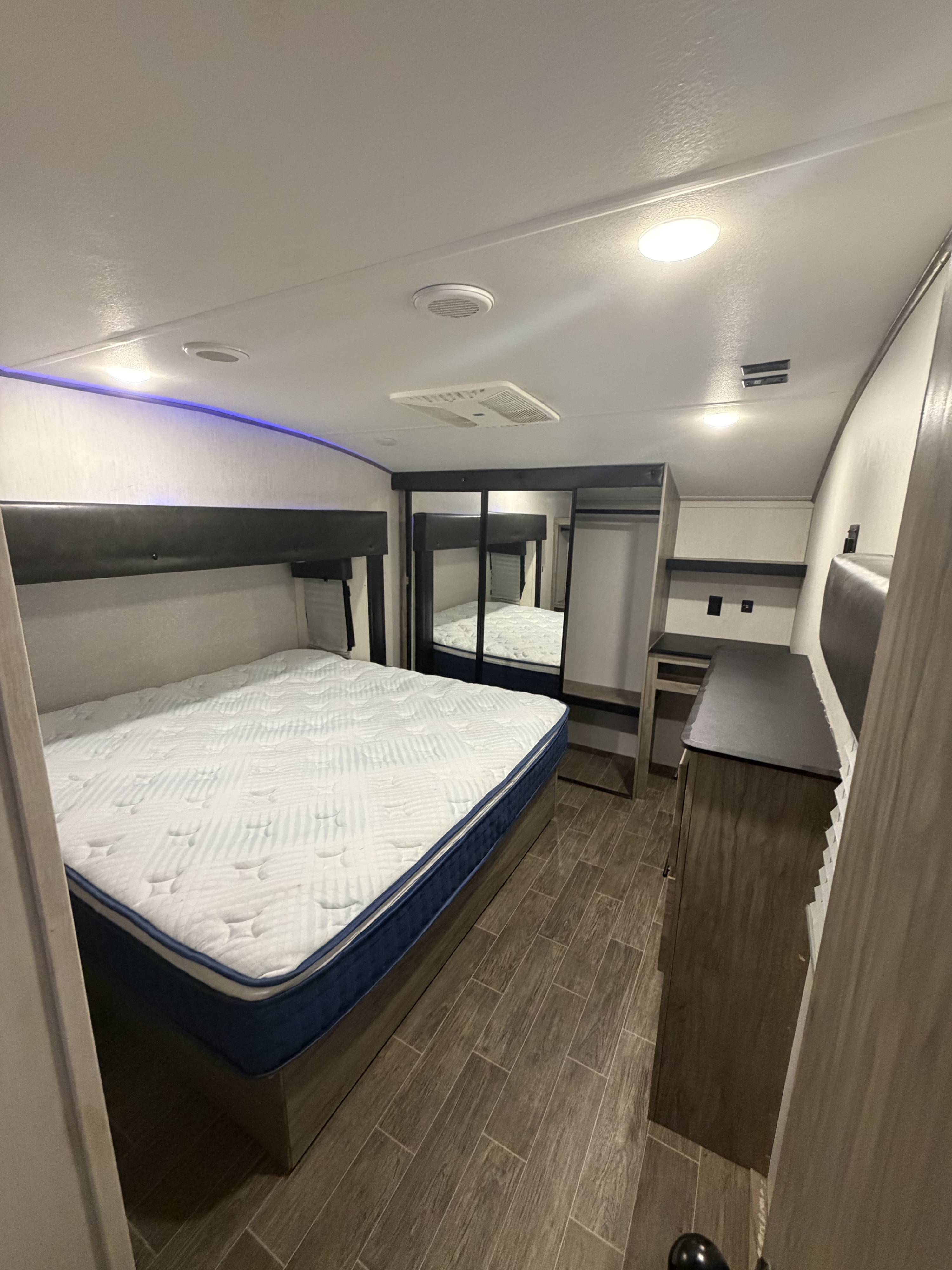 Spacious RV rental bedroom featuring a queen bed, wood floors, mirrored closet, ceiling AC, and accent lighting.. Forest River Artic wolf 2022