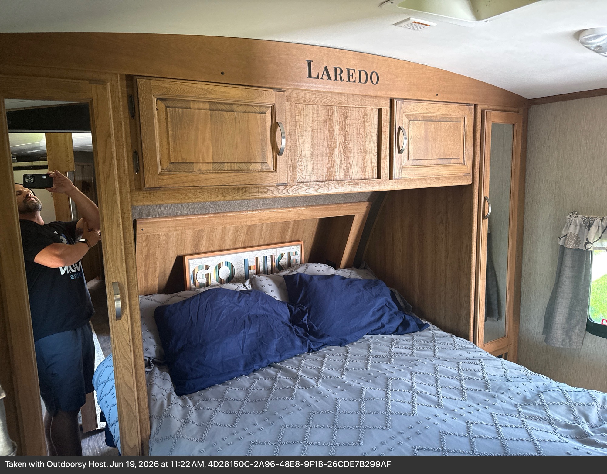 Laredo RV rental bedroom with a bed, "GO HIKE" sign, overhead cabinets, and mirrored closet, offering comfortable storage.. Keystone RV Laredo 2015