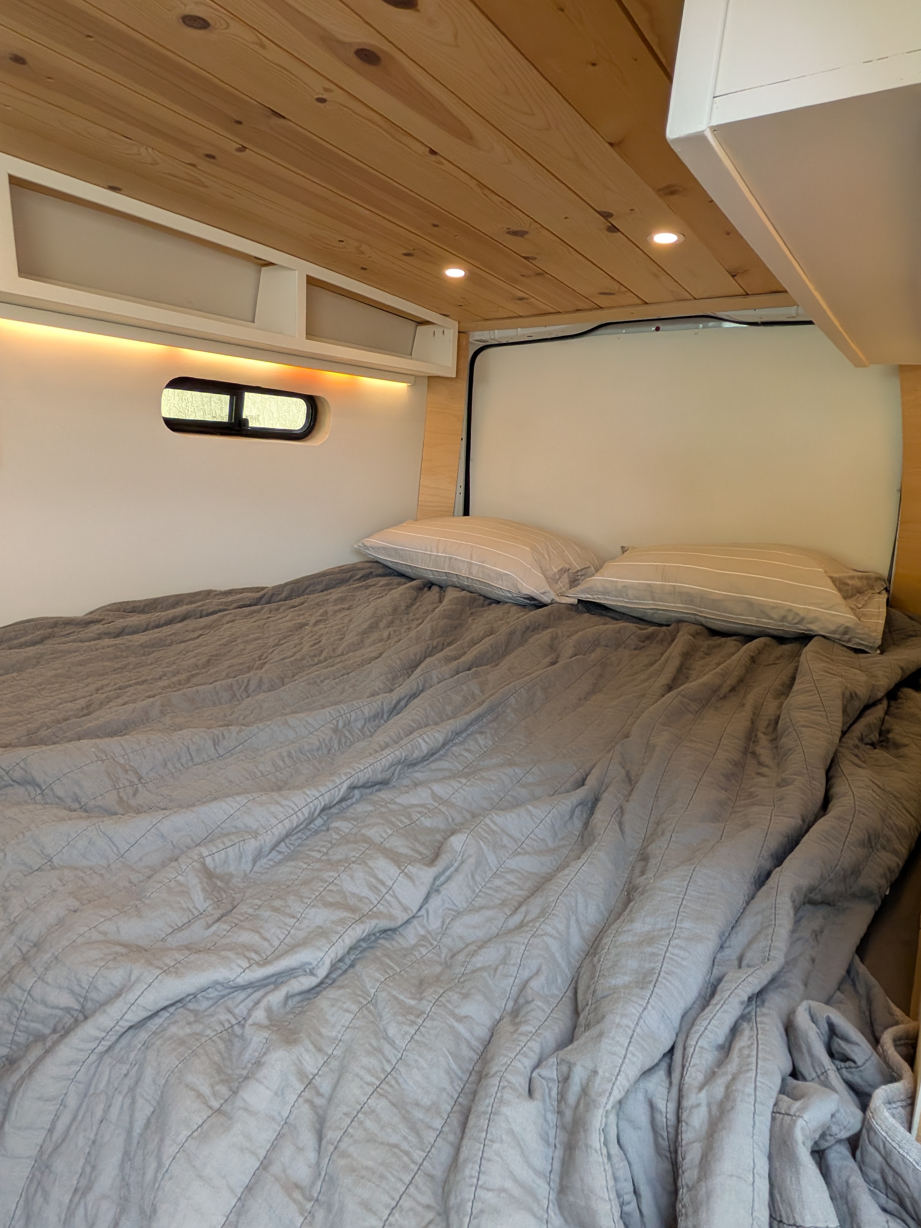 Cozy camper van bedroom in an RV rental, featuring a wood ceiling, soft lighting, and a comfortable bed with pillows.. Mercedes-Benz Metris Turbo 2021