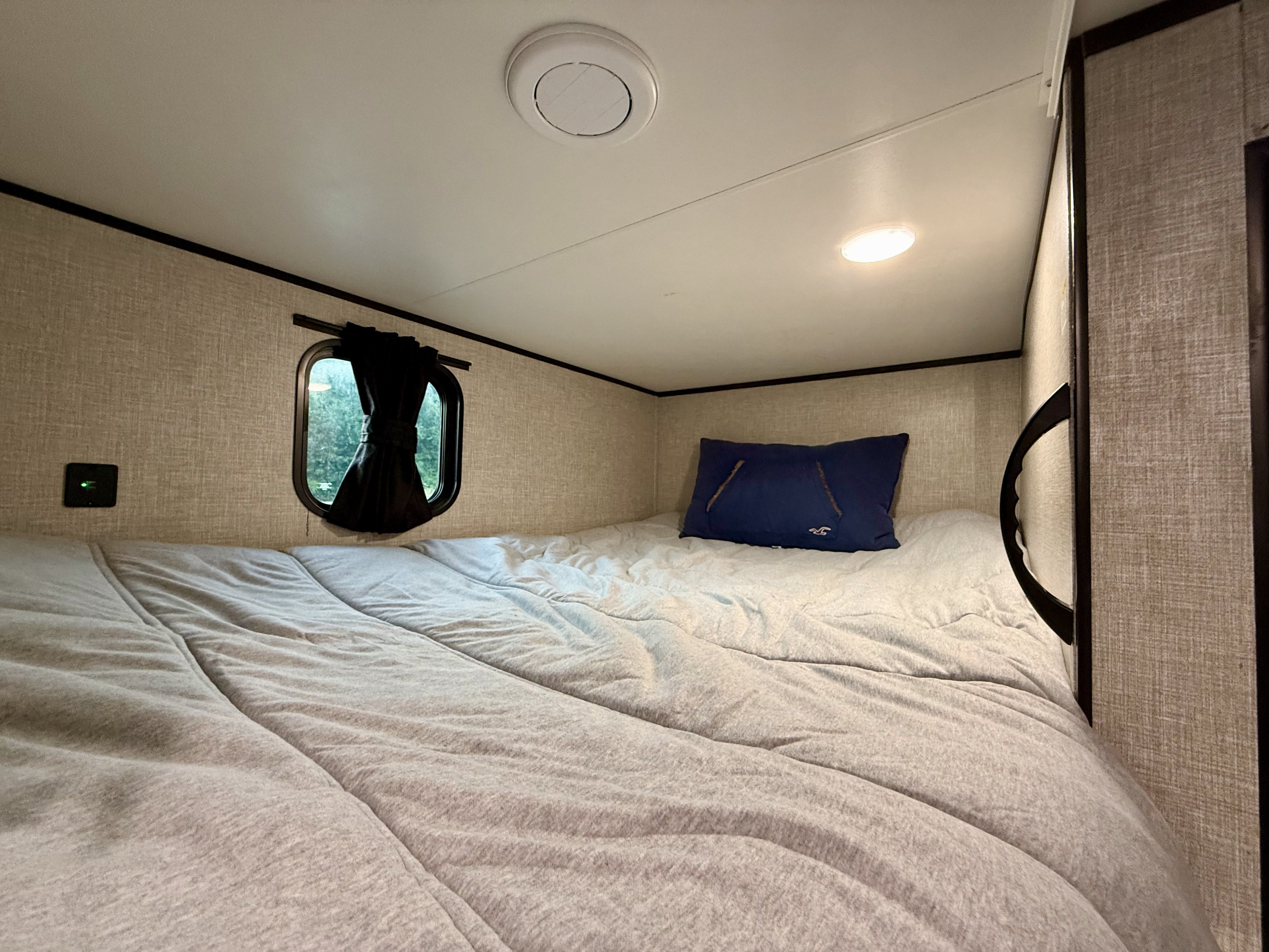 Cozy RV rental bunk bed with textured walls, a small window, and soft bedding, featuring a blue pillow and overhead lighting.. Jayco Jay Flight SLX 2022