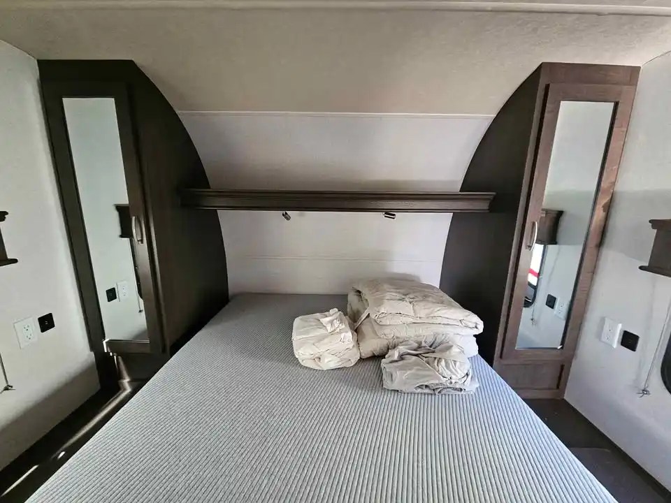 This inviting RV rental bedroom features a comfy bed, mirrored wardrobes, and an overhead shelf, ready for your travels.. Forest River Shockwave 2019