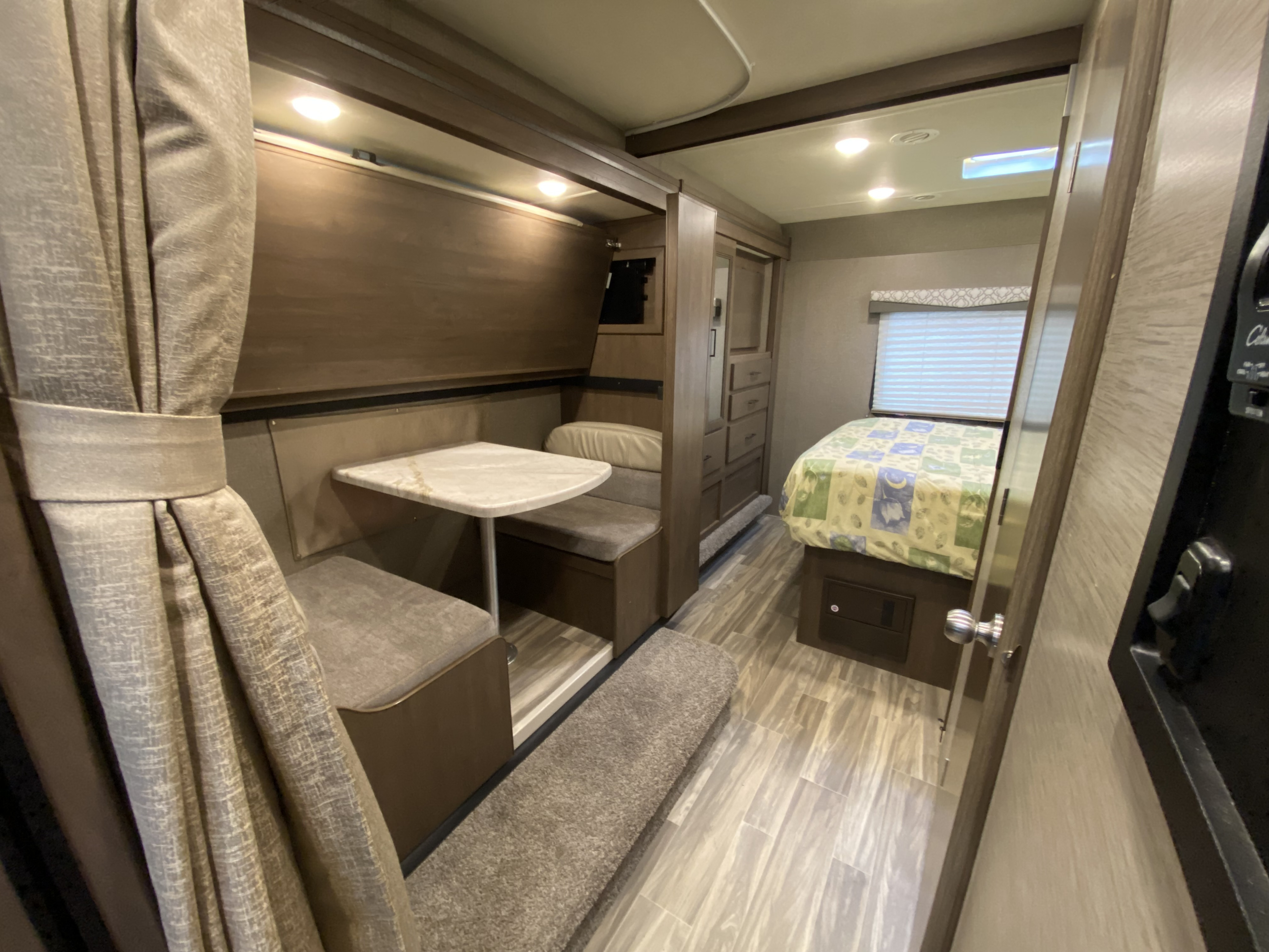 Modern rv rental interior: dinette on left, bed on right, storage in between. Light wood accents, carpet & vinyl floor.. Thor Freedom Elite 2021