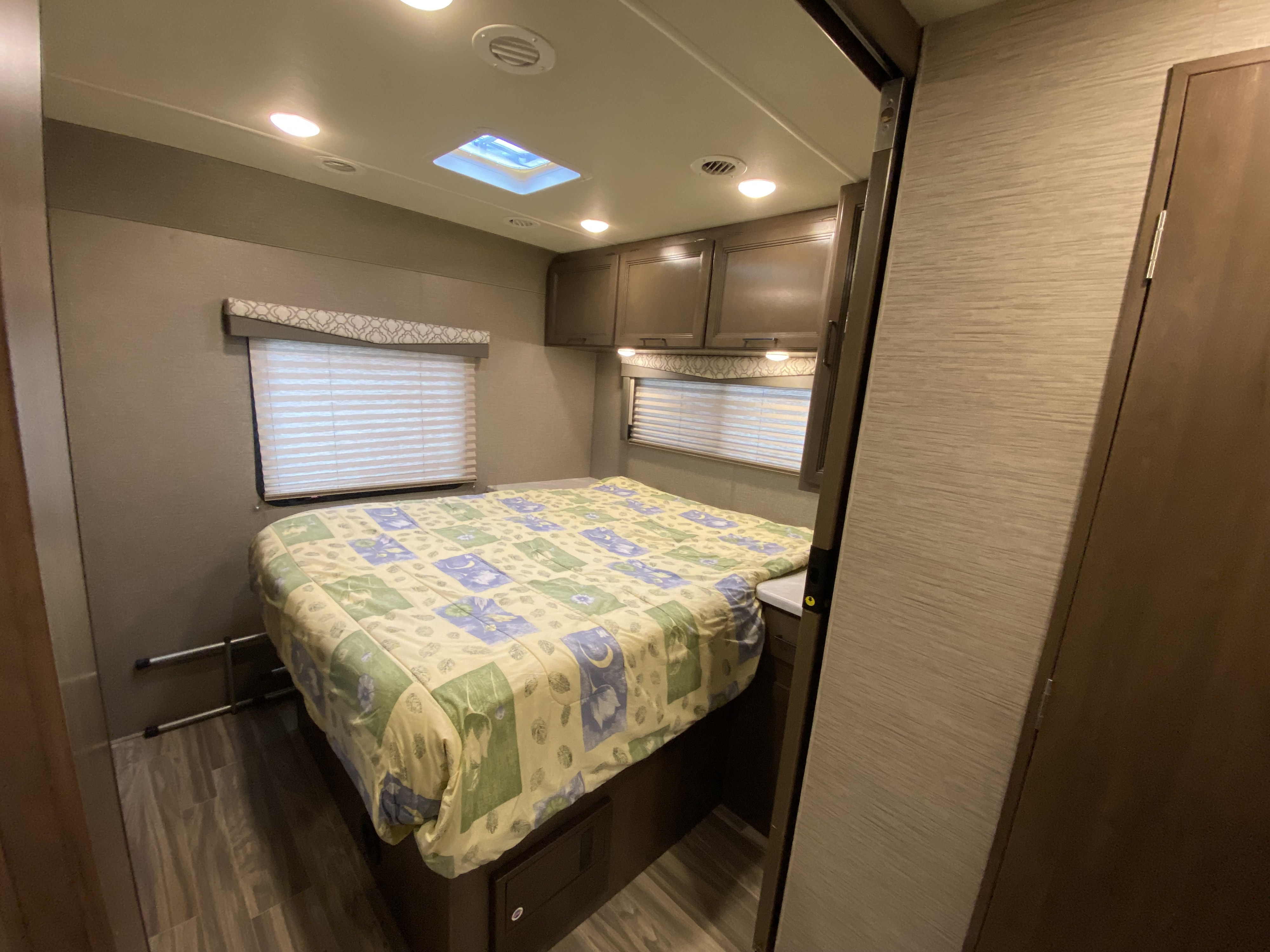 A neat RV rental bedroom with a comfy bed, windows with blinds, and ample overhead cabinets. Ideal for road trips.. Thor Freedom Elite 2021