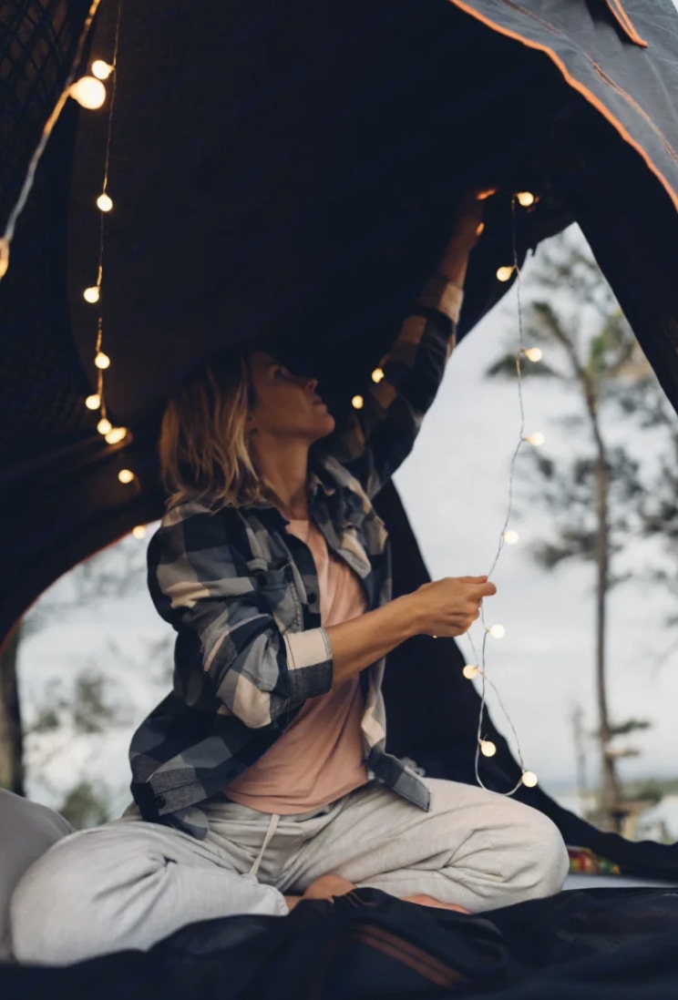 A woman decorates her RV rental interior with twinkling fairy lights, creating a warm, inviting camp setup.. Toyota FJ Cruiser 2011