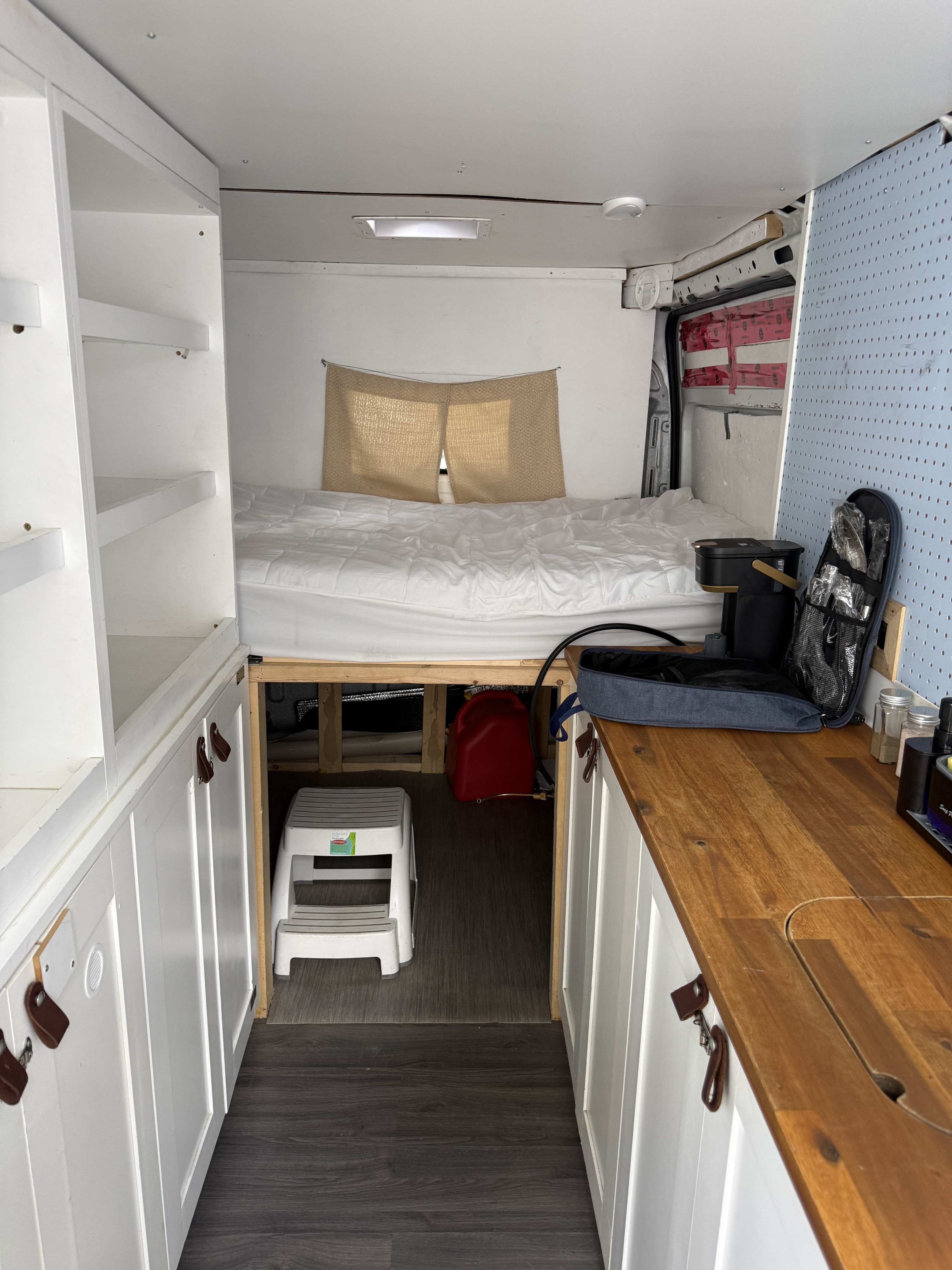 RV rental campervan interior with bed, compact kitchen with wood counter, white storage, and dark flooring.. Dodge Ram 3500 pro master 2014