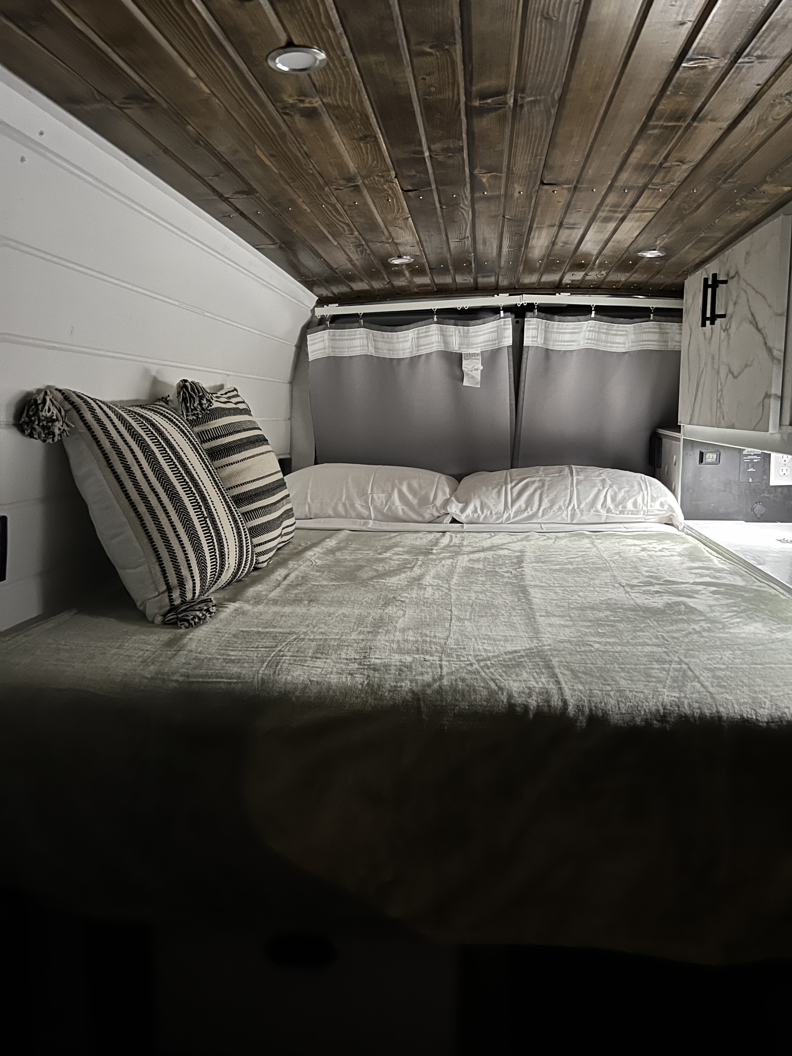 Cozy RV rental bedroom with a wooden ceiling, white walls, comfortable bed, and stylish striped pillows.. Ford Ford E350 2005