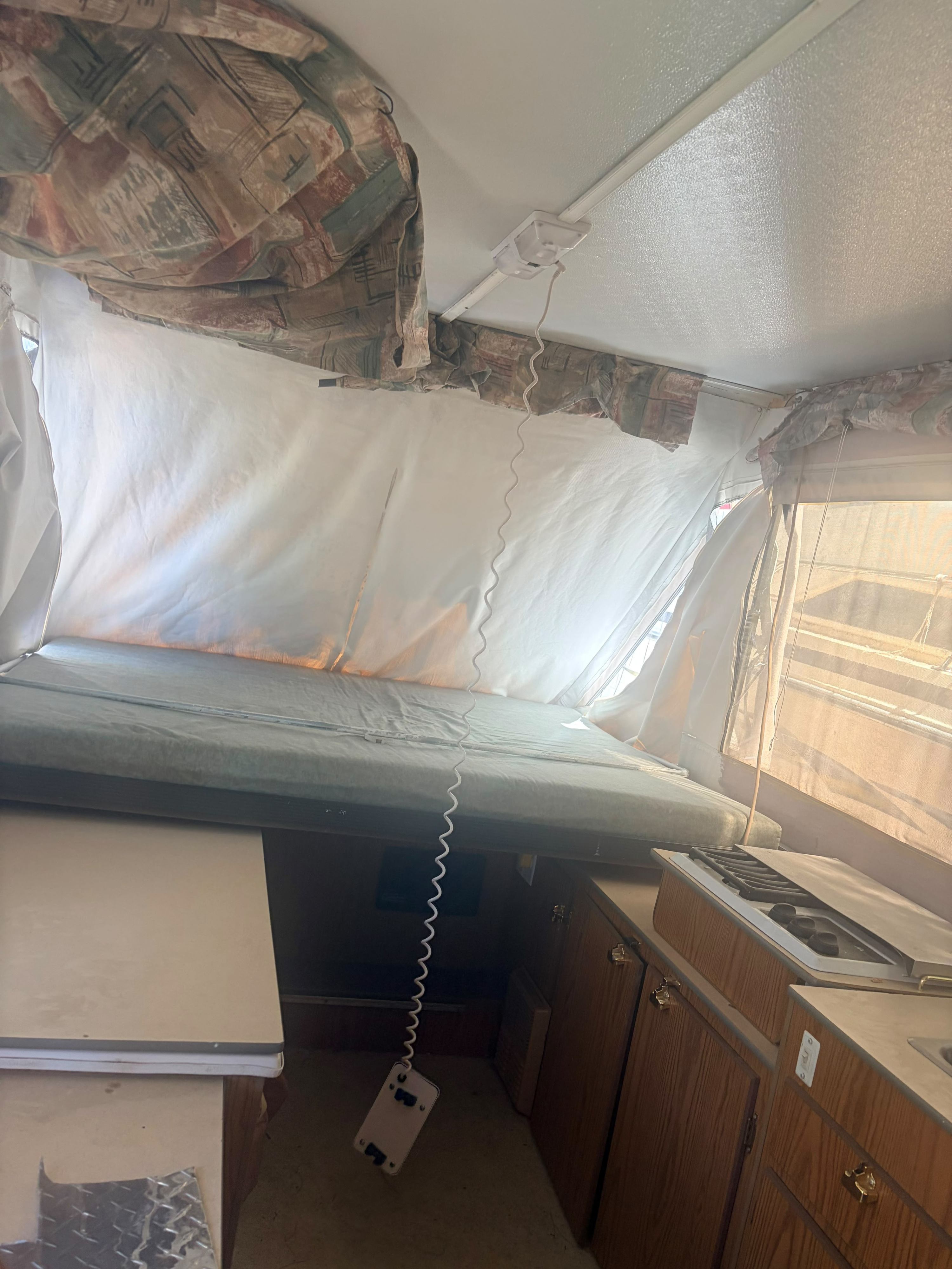 Interior of a pop-up camper RV rental, featuring a bed with fabric walls, ceiling light, and compact kitchen with stove.. Jayco eagle 1999 1999