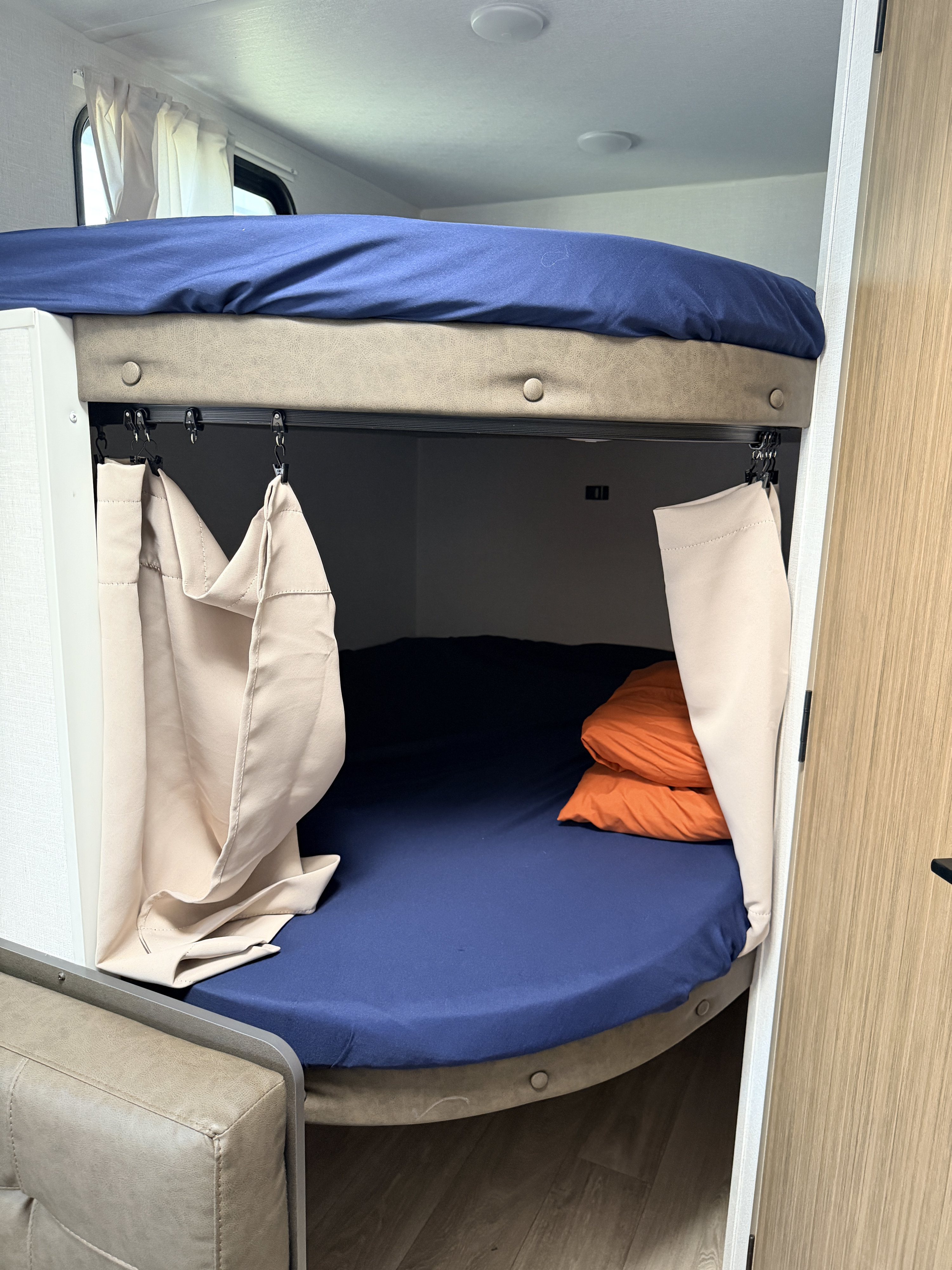 RV rental features double bunk beds with blue sheets and privacy curtains. A cozy camper sleeping area with orange pillows.. Forest River Wildwood FSX 2026