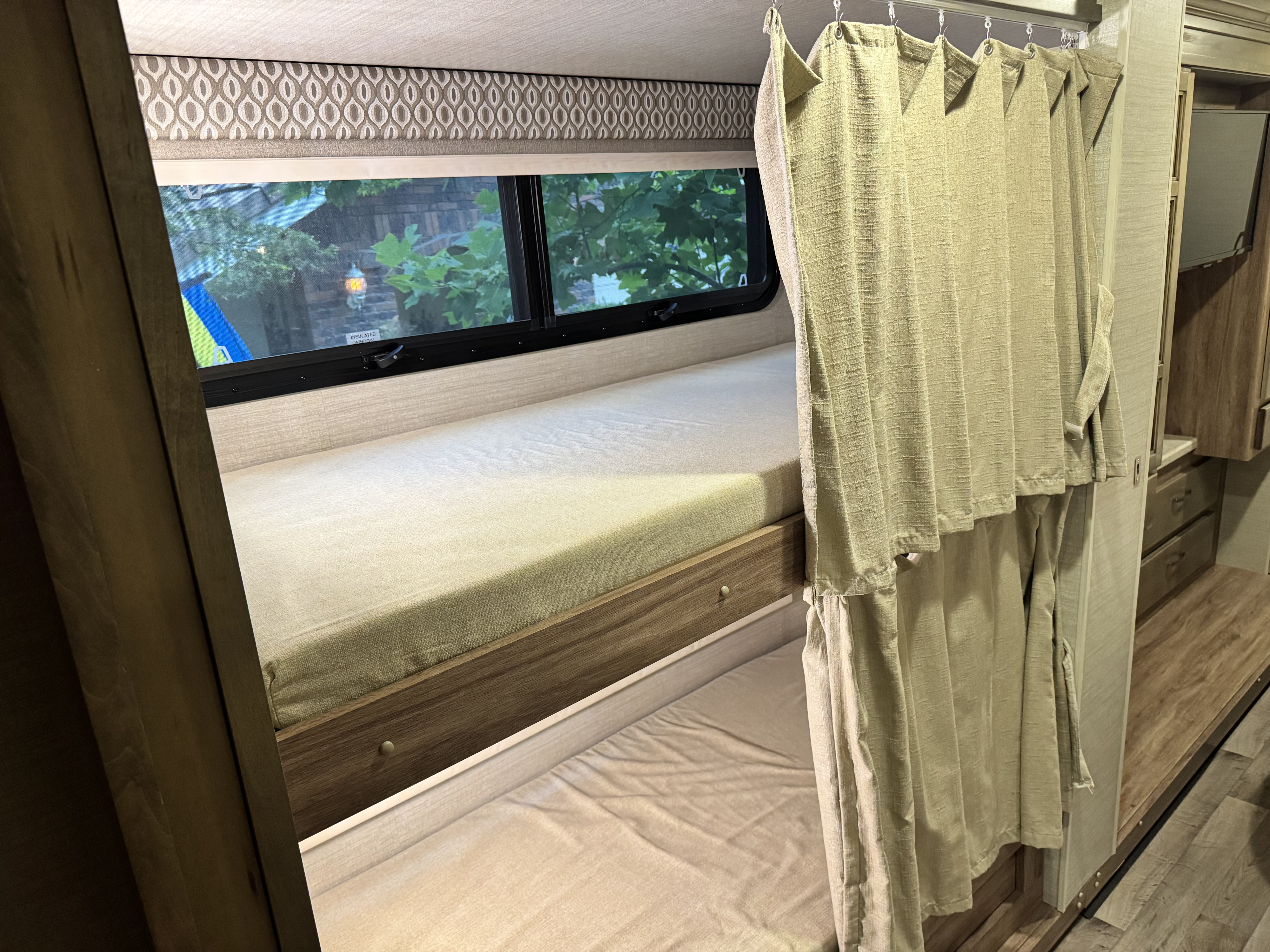 Inside an RV rental: two cozy bunk beds with a window overlooking trees and a privacy curtain for comfortable travel.. Jayco Precept 2019
