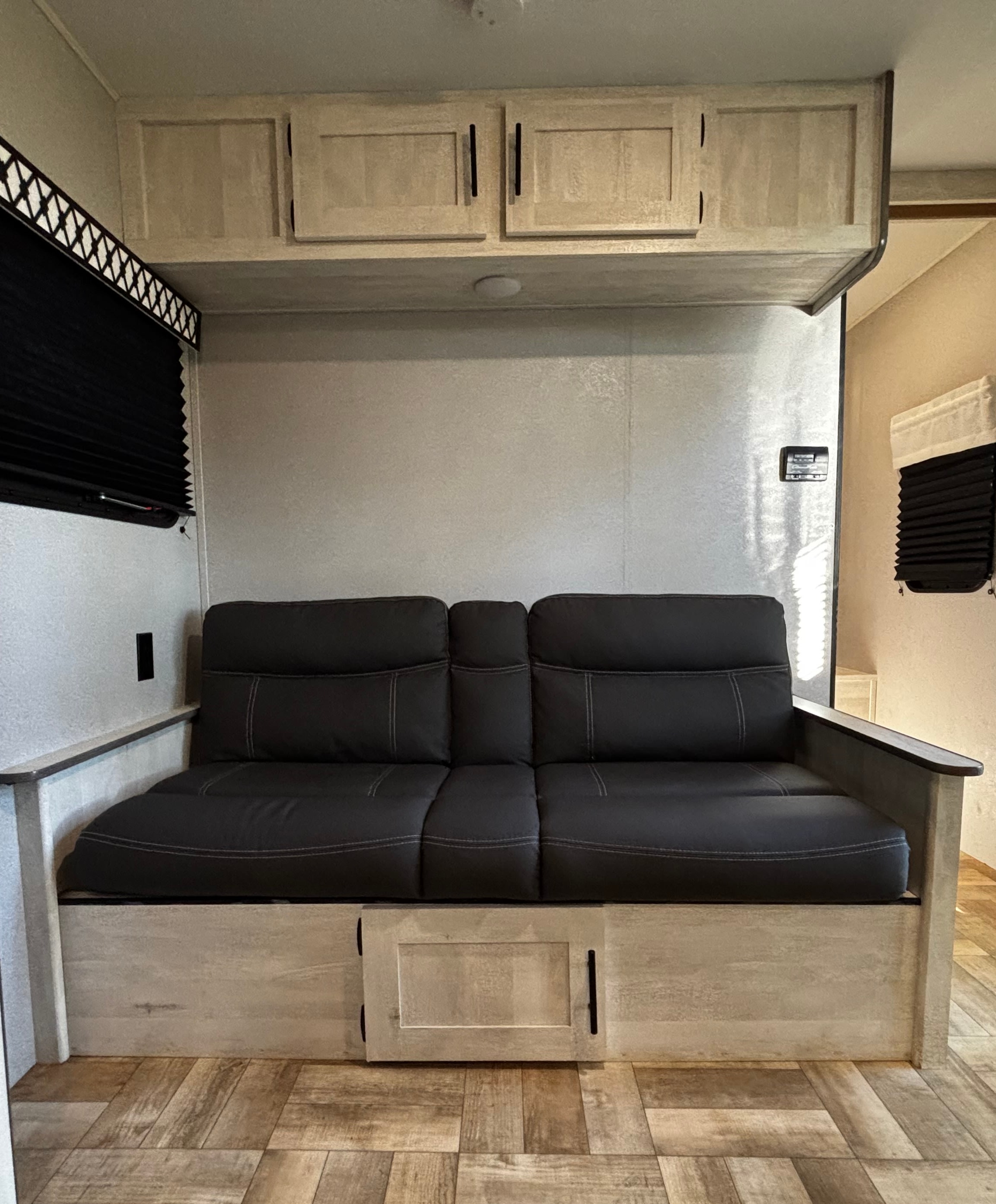 Inside an RV rental: a comfortable dark sofa with overhead cabinets and wood flooring. Perfect for your road trip!. Forest River Shasta 2022