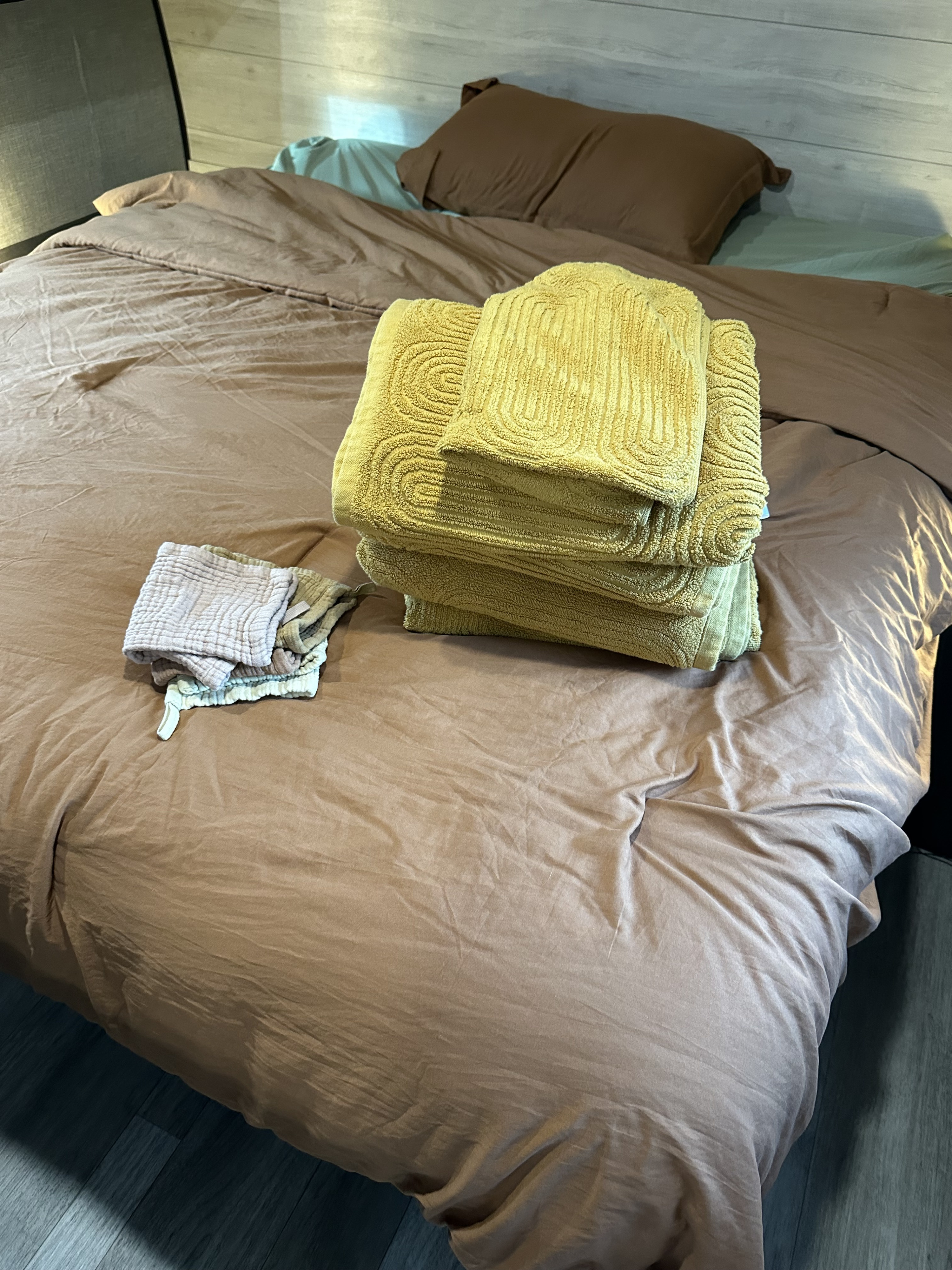 Cozy RV rental bedroom with a brown duvet, stacked yellow textured towels, and smaller folded cloths on the bed.. Jayco Jay Flight 2023
