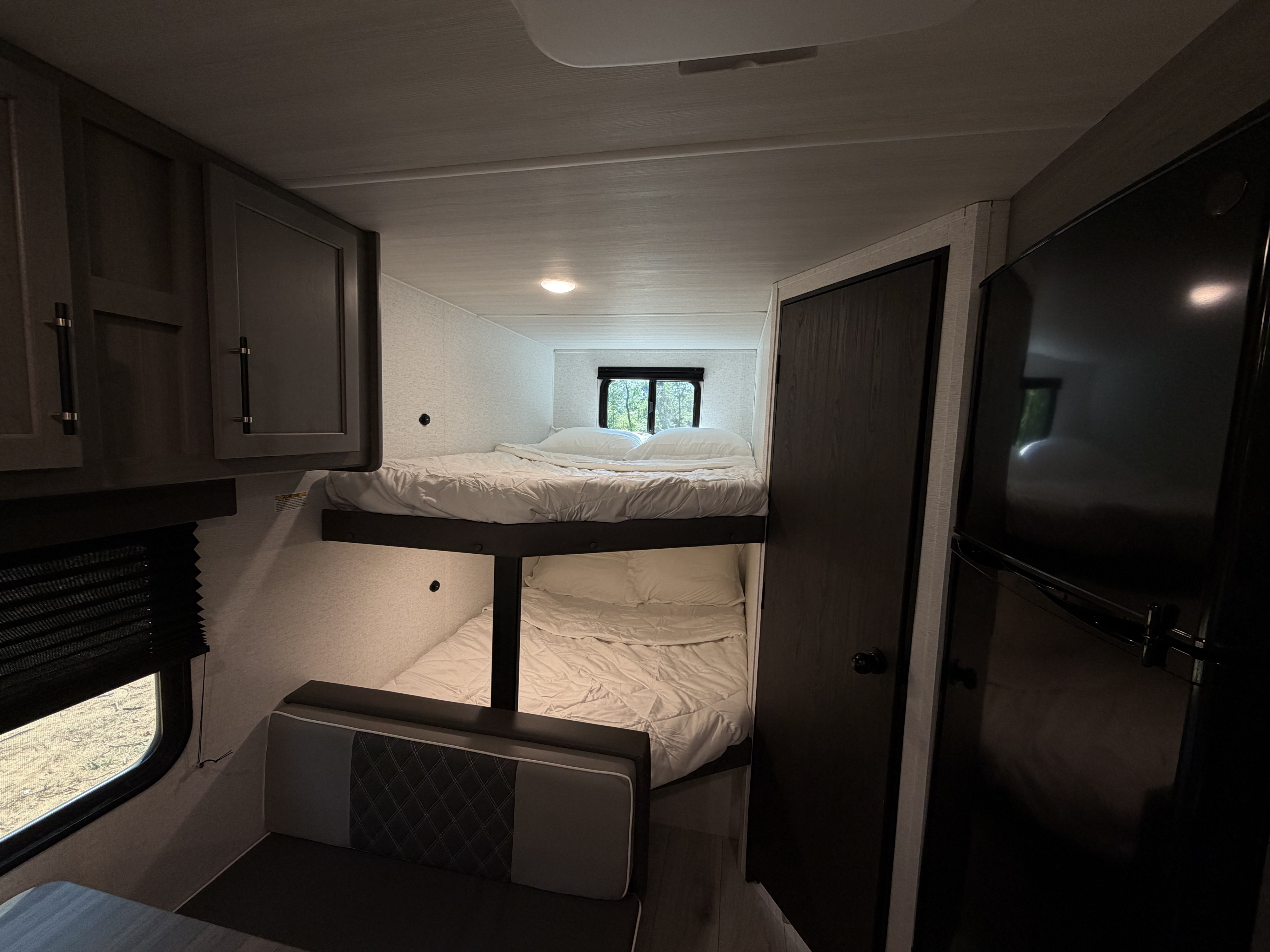 Bright RV rental interior with comfortable bunk beds, dinette seating, kitchen cabinets, and a scenic window view.. Keystone RV Hideout Sport 2025