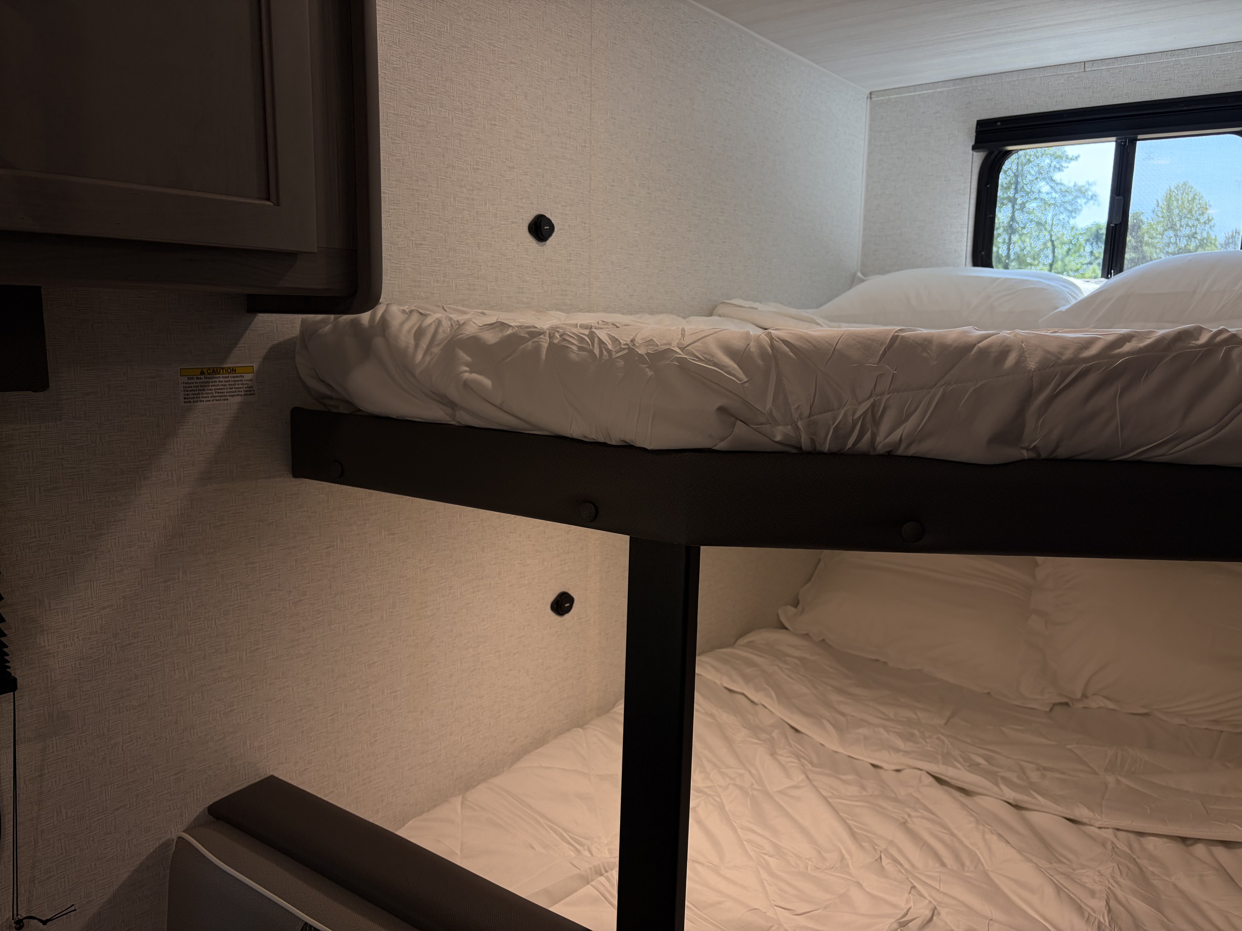 Cozy RV rental bunk beds with white bedding, offering comfortable sleeping quarters and a window view to nature outside.. Keystone RV Hideout Sport 2025