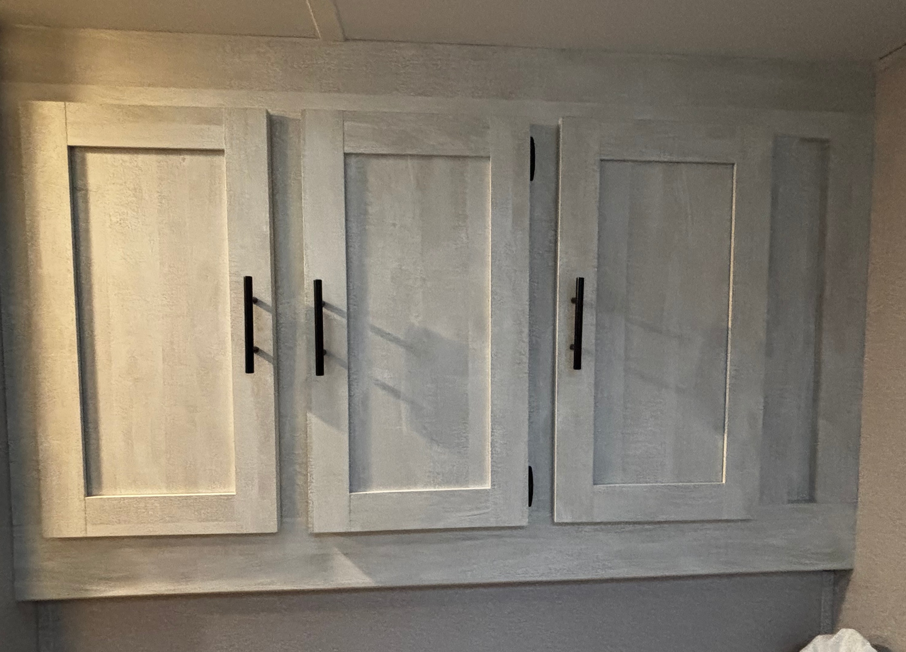 RV rental interior: three light-toned overhead cabinets with black bar handles, offering convenient storage.. Forest River Shasta 2022