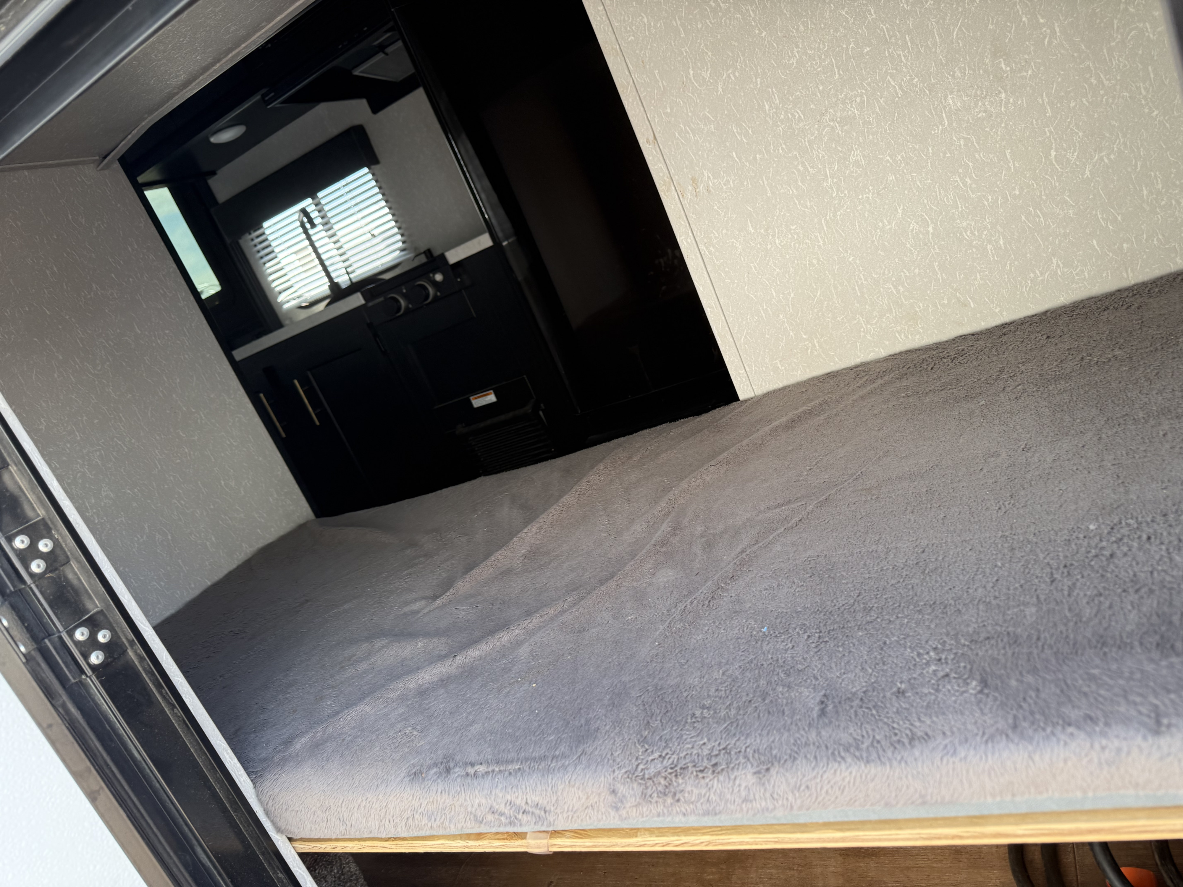 RV rental interior: A cozy bunk bed with grey blanket in foreground, with a peek into a kitchen area with sink & window beyond.. Forest River Cherokee Wolf Pup 2021
