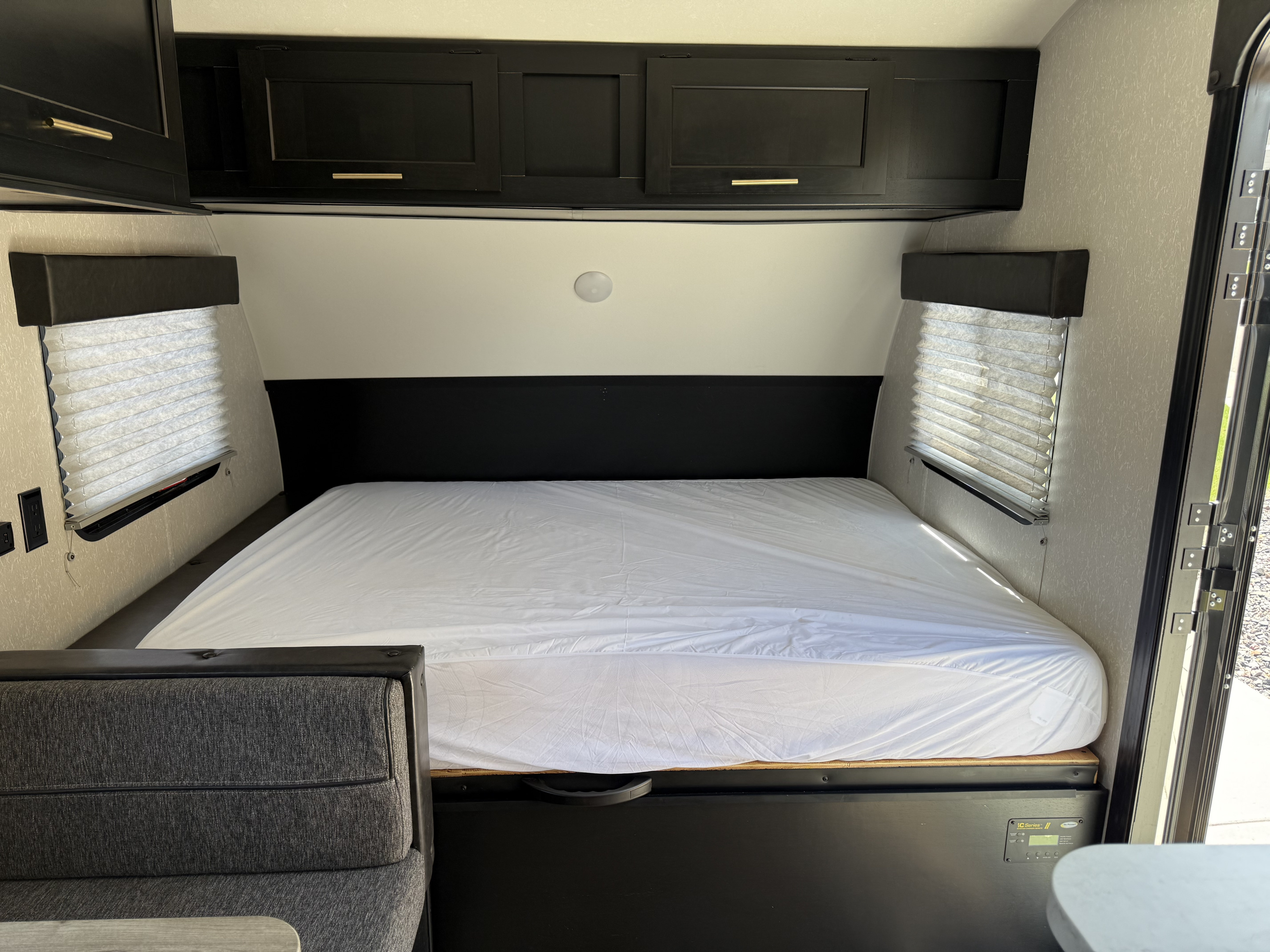 Inside this modern RV rental: a clean bedroom with a full bed, black overhead cabinets, and window blinds.. Forest River Cherokee Wolf Pup 2021