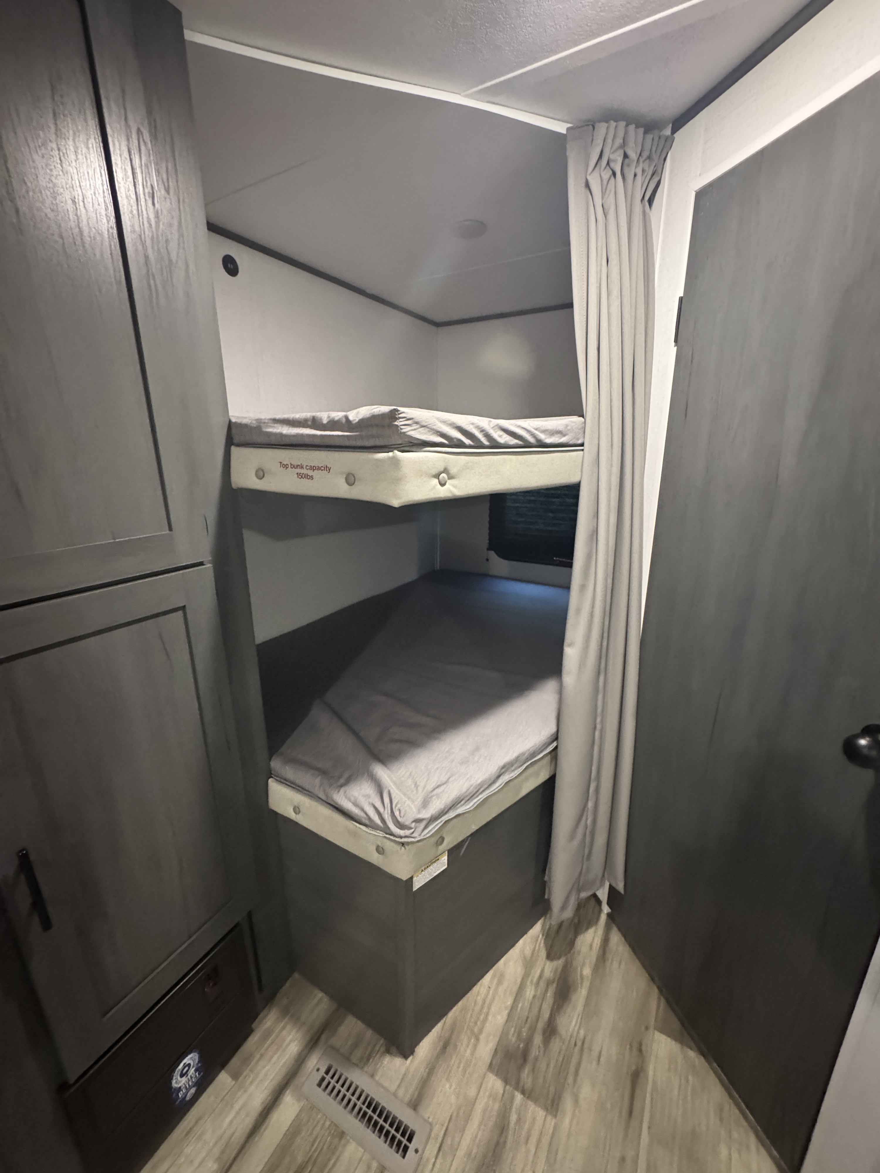 Cozy bunk beds in an rv rental, featuring two beds, a privacy curtain, and adjacent storage. Top bunk capacity is 150 lbs.. Dutchmen Colorado 2024