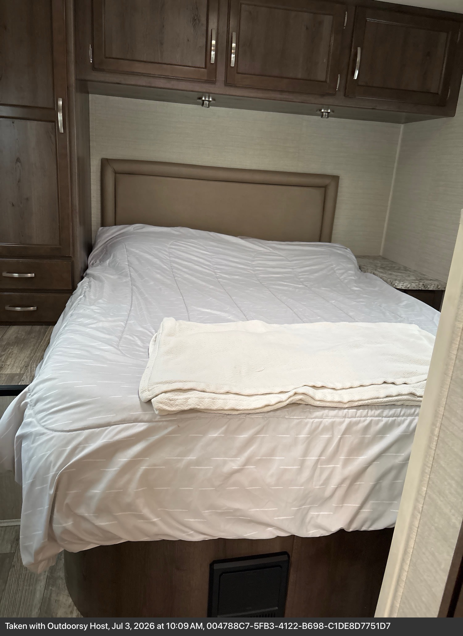 A comfortable RV rental bedroom featuring a neatly made bed with a headboard, overhead cabinets, and side storage.. Jayco Redhawk 2018