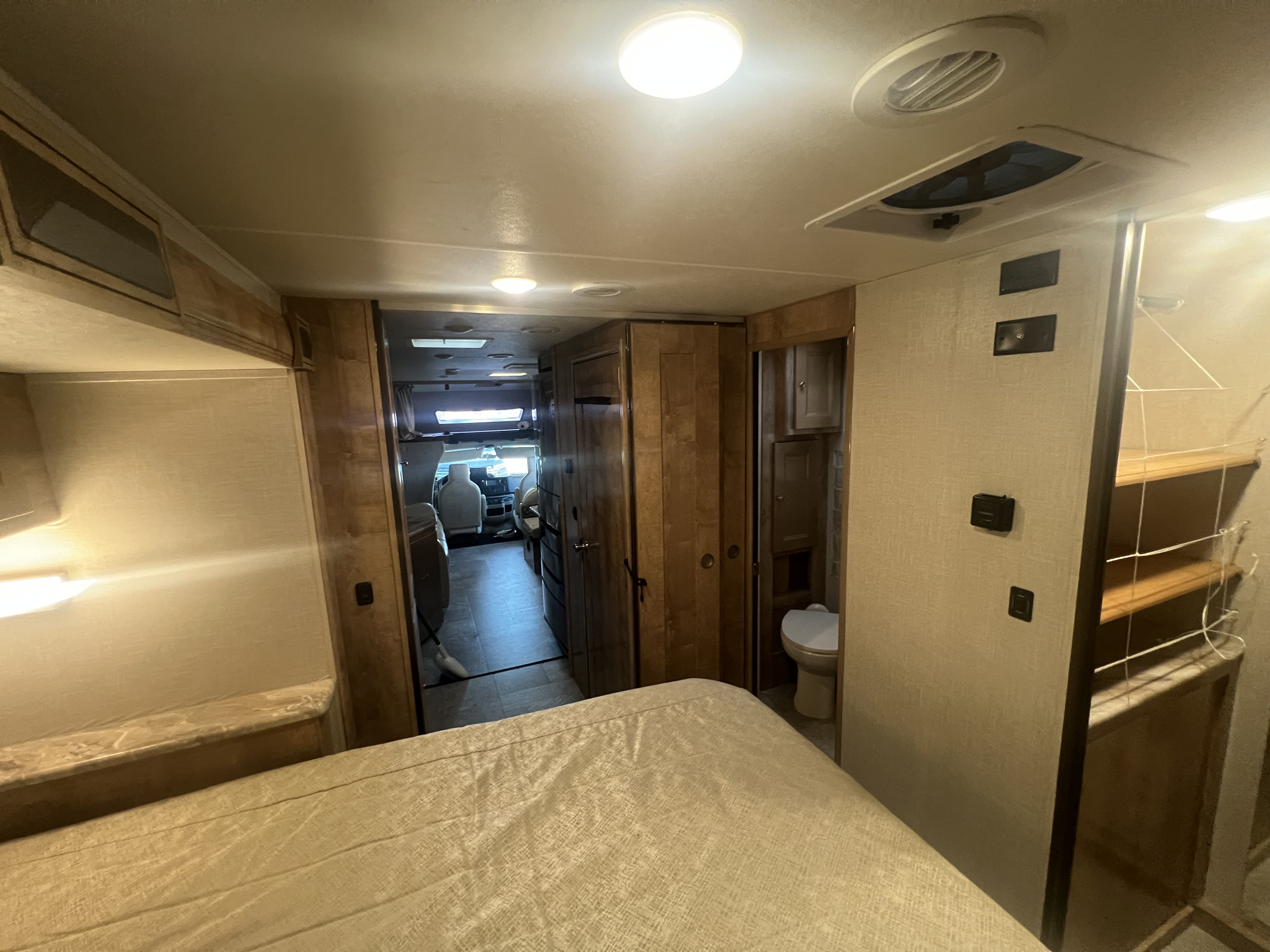 Cozy RV rental interior with a comfortable bed, a hallway leading to the cockpit, and a compact bathroom. Ideal for travel.. Forest River Coachmen Leprechaun 2020