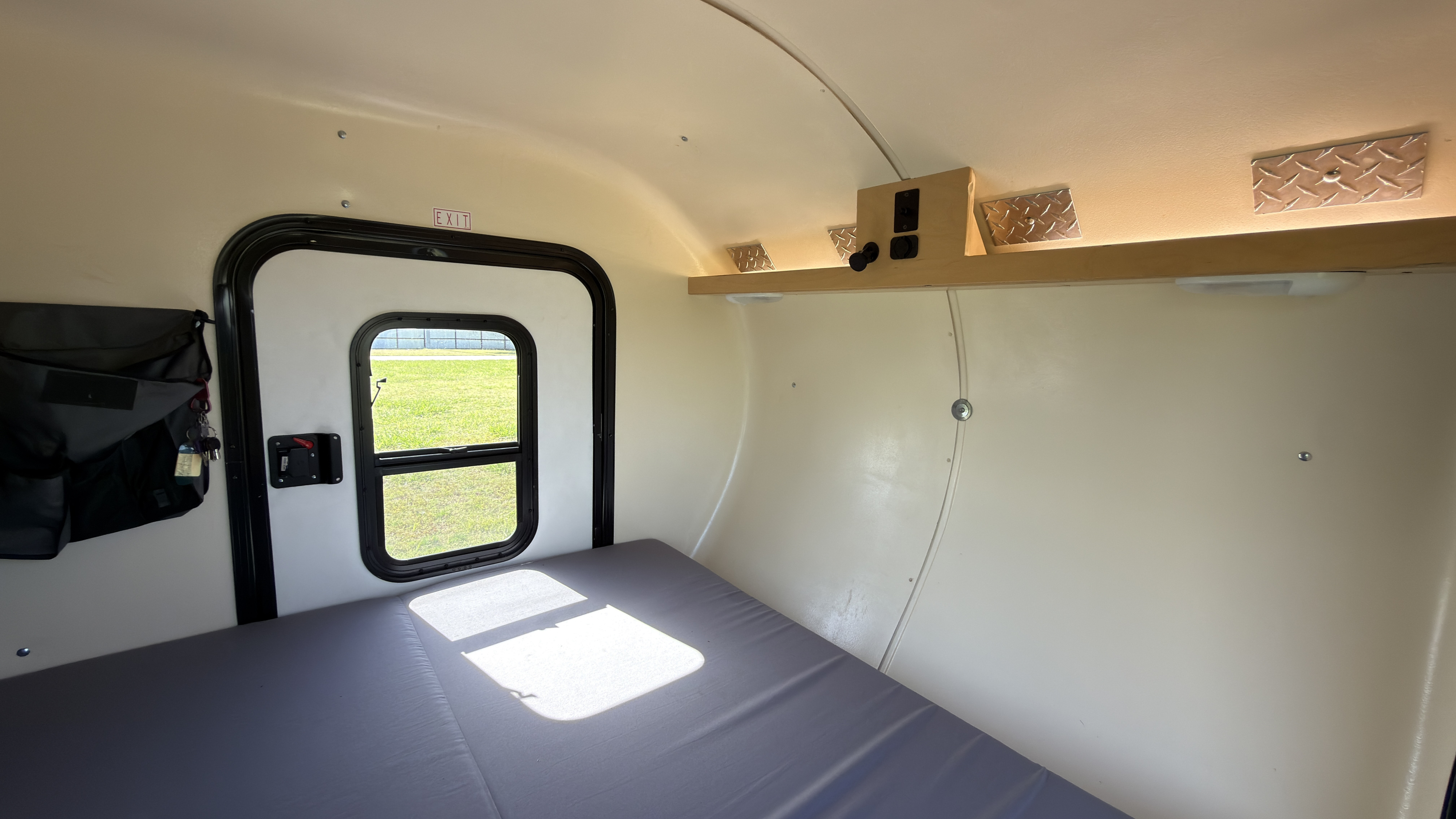 Compact rv rental interior with a bed, exit door, and overhead shelf with controls. Ready for your adventure.. High Altitude XT50 Treardrop Camper 2022