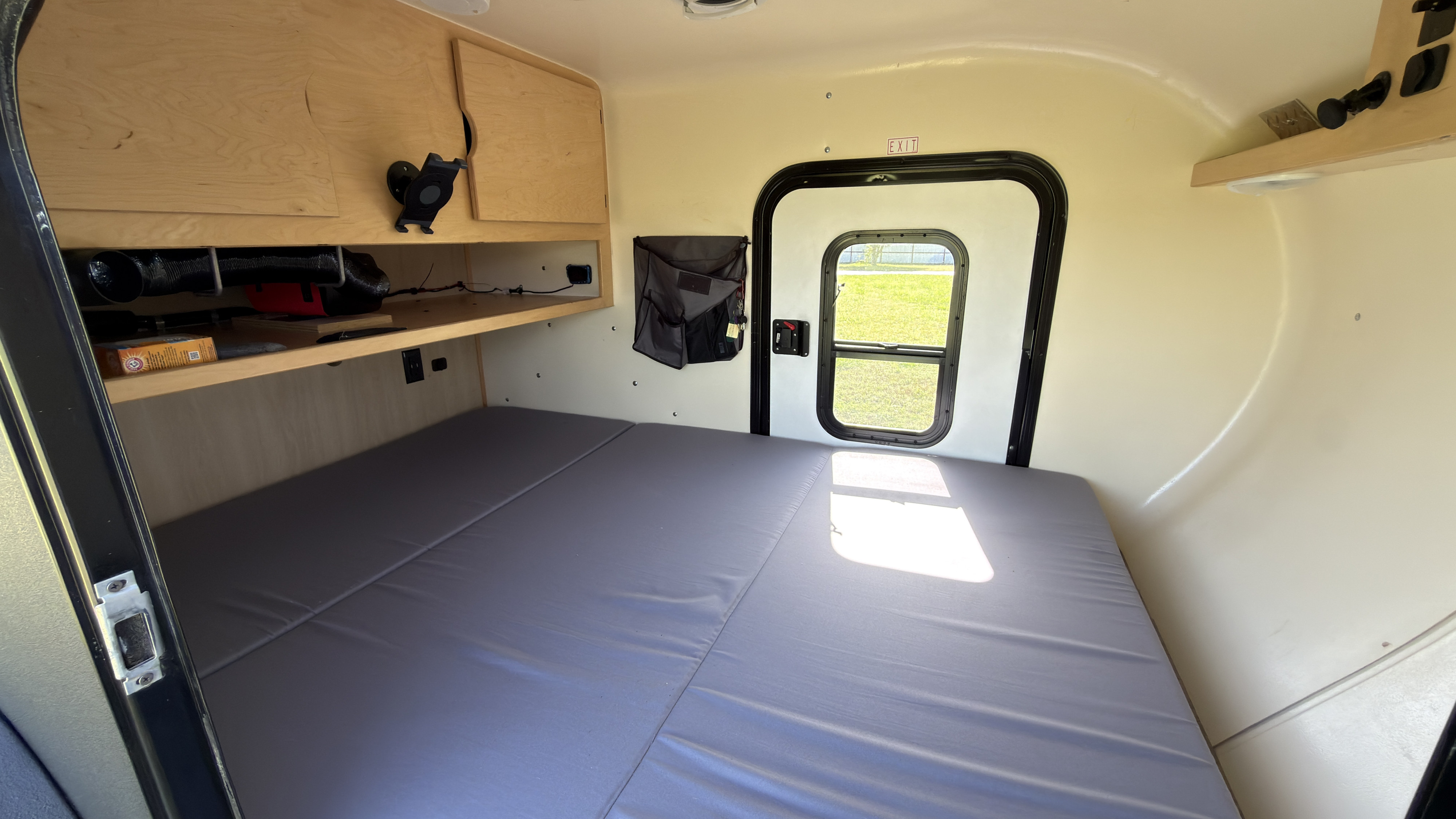 RV rental interior: wide bed, wooden cabinets, and rear exit door with view to outside grass.. High Altitude XT50 Treardrop Camper 2022