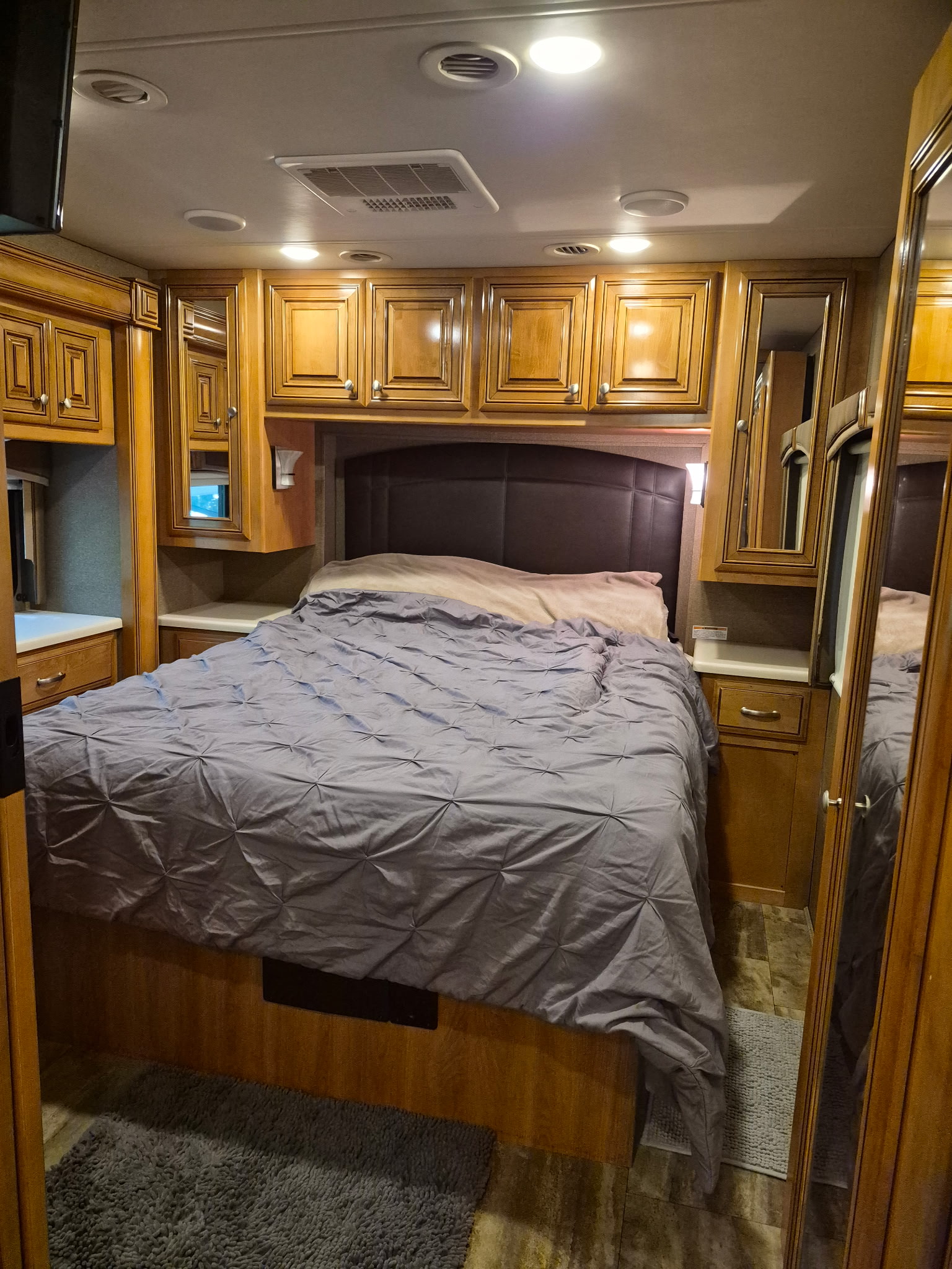 Cozy rv rental bedroom features a comfortable bed, warm wooden cabinetry, and bright overhead lighting.. Thor Palazzo 2018