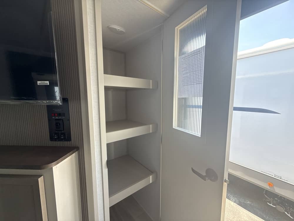 RV rental interior: TV, control panel, and a spacious pantry with shelves. The door opens to bright outdoor light, showing another camper.. Forest River Salem Hemisphere HL 2025