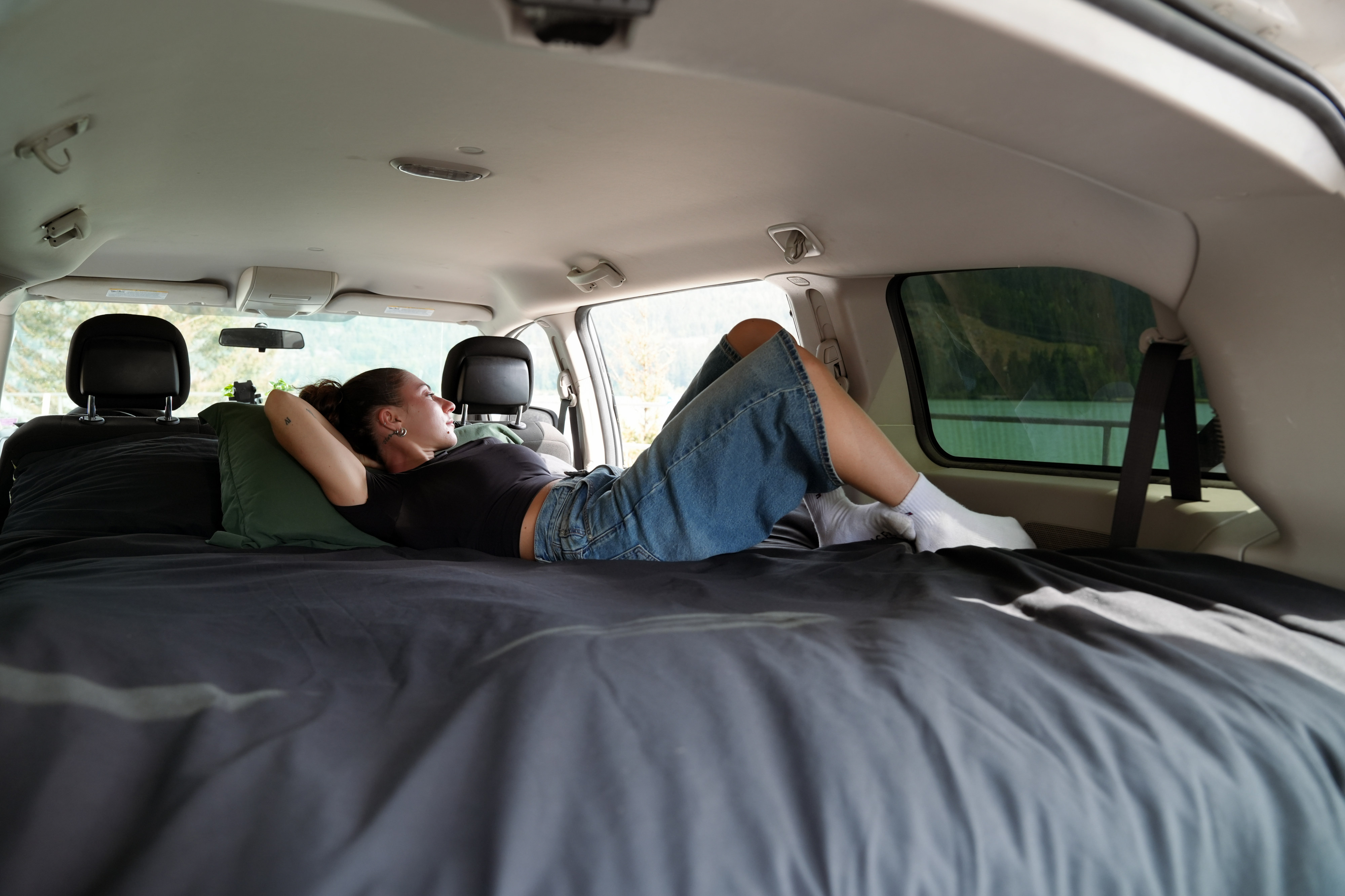 Woman relaxing on a comfy bed inside an RV rental. She enjoys the scenic view from the vehicle's spacious interior.. Dodge B Van 2014