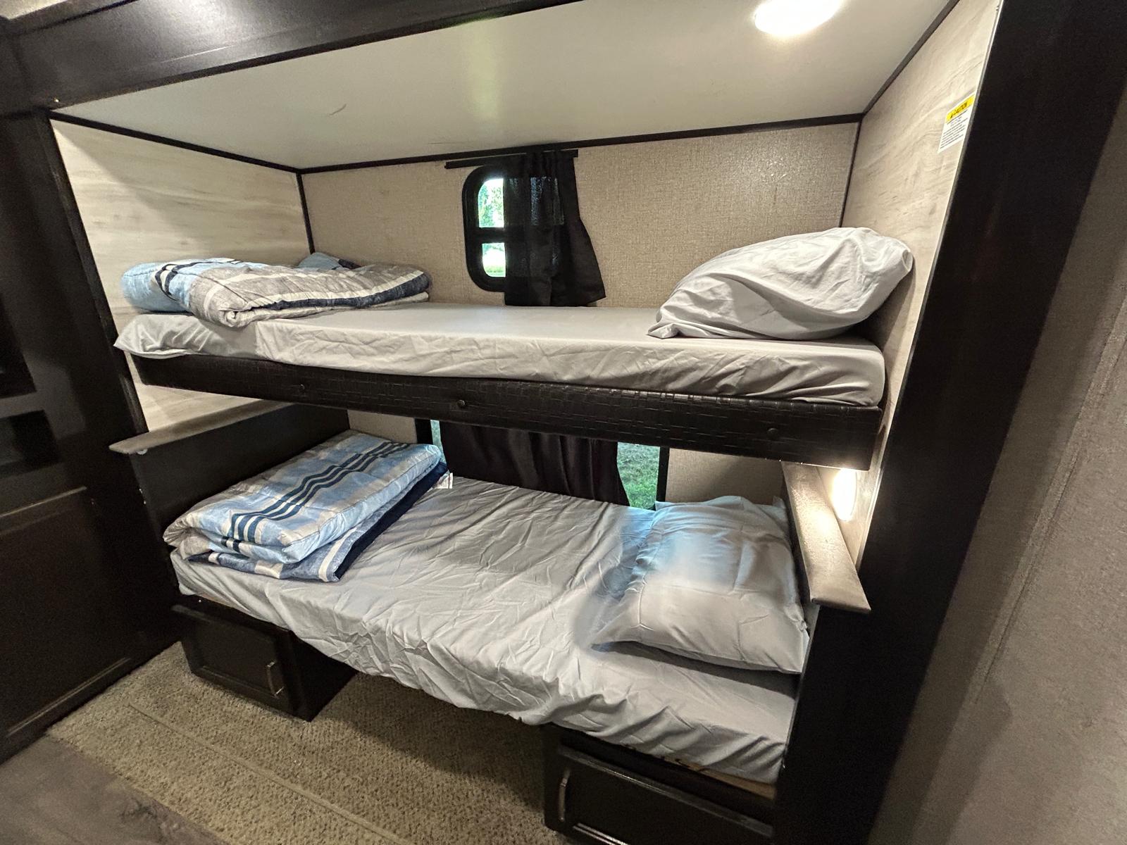 Cozy RV rental bunk beds. Two beds, each with bedding, visible inside an RV, with a window between them.. Jayco Jay Flight 2021