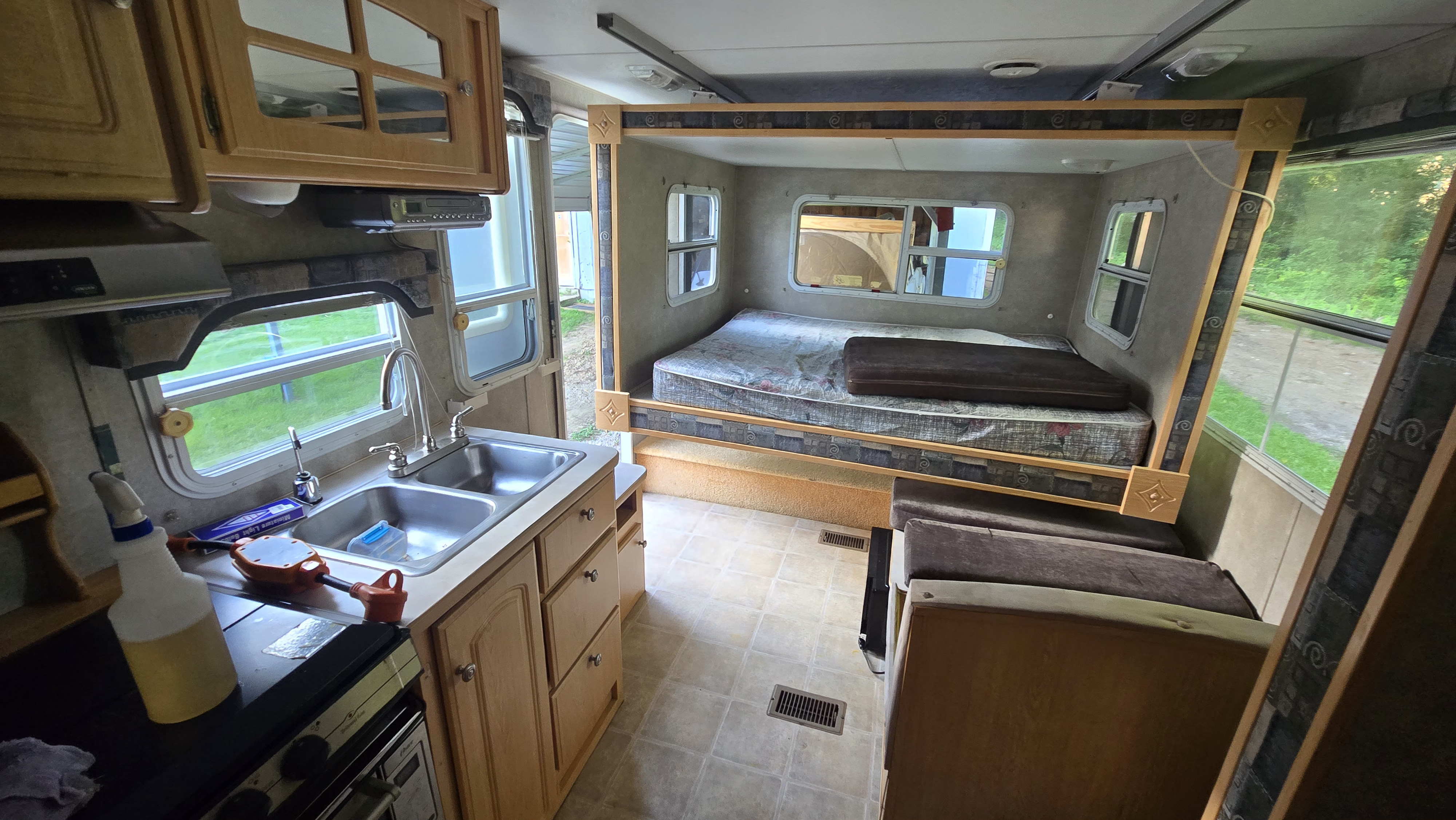 RV rental interior showing a kitchen with sink, stove, and cabinets, adjacent to a cozy sleeping alcove with a bed.. Starcraft Homestead Settler 2004