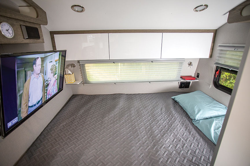 Cozy RV rental bedroom with a comfortable bed, mounted TV, overhead storage, and windows for a relaxing travel experience.. InTech RV InTech RV Trailer 2021