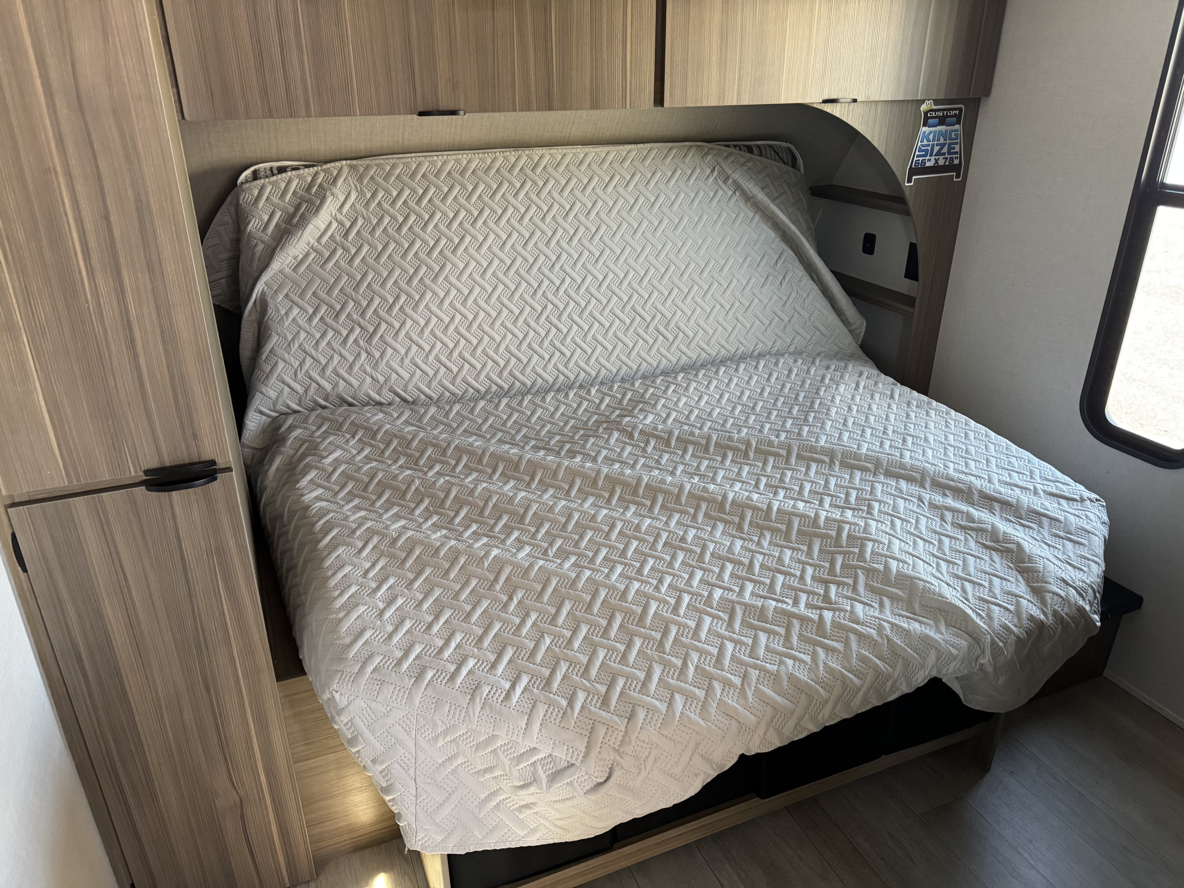 Compact RV rental bedroom featuring a custom king-size bed with a quilted bedspread & surrounding storage cabinets.. Forest River Salem Cruise-Lite 2025