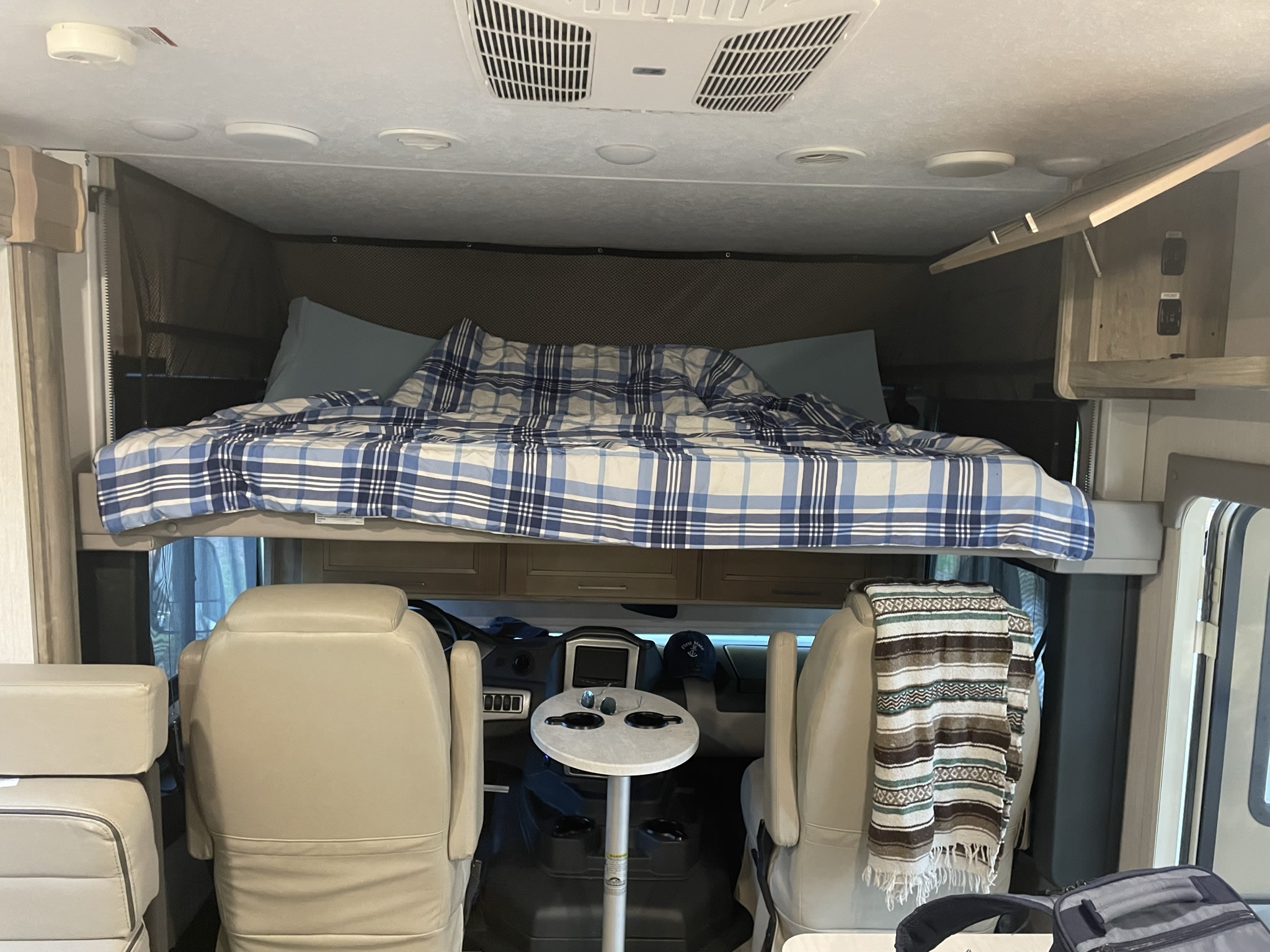 This rv rental features a cozy overhead bed with plaid bedding, visible above the front cockpit and seats.. Coachmen Mirada 32ss 2020