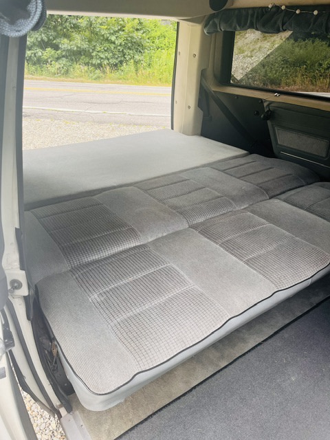 Cozy camper van interior for your next RV rental. Features a comfortable convertible bed/seating area with grey upholstery.. Volkswagen Vanagon 1990