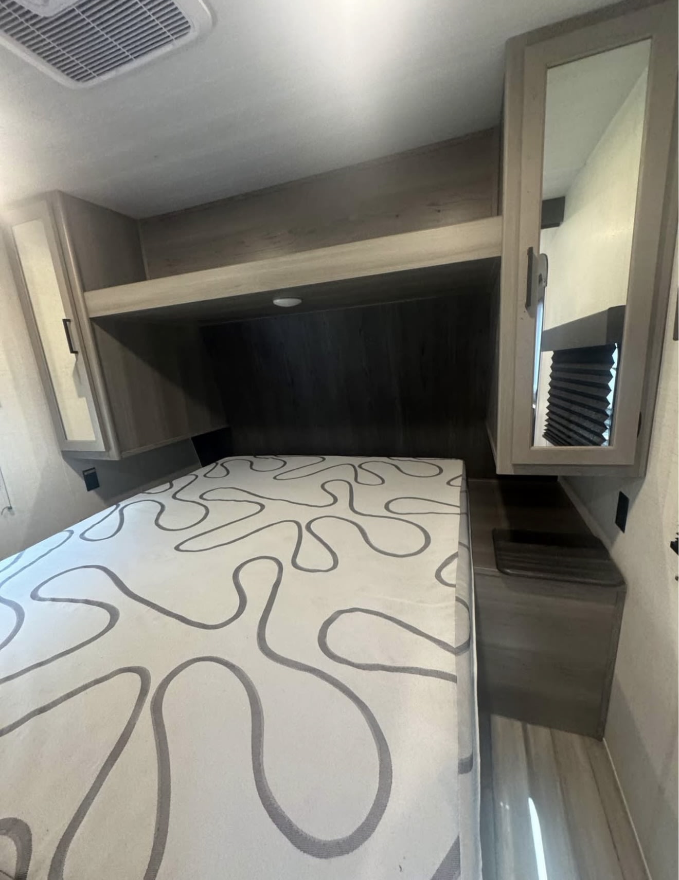 RV rental bedroom interior: a comfy bed with a patterned mattress, overhead storage, and mirrored cabinet. Ideal for travel!. Keystone RV Hideout 2024