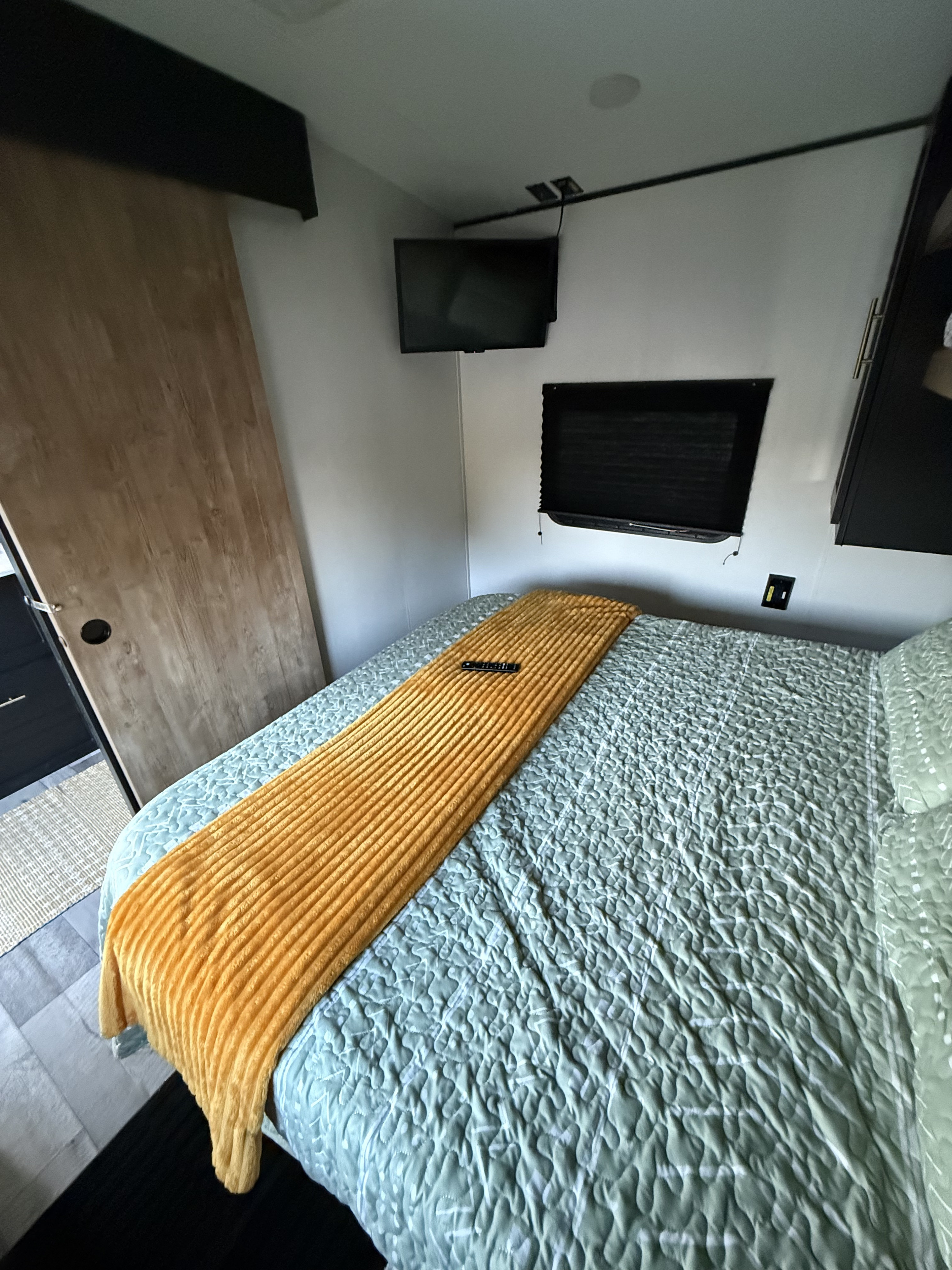 RV rental bedroom featuring a cozy bed with green quilt, orange throw, wall TV, and modern dark accents.. Keystone RV Springdale 2022