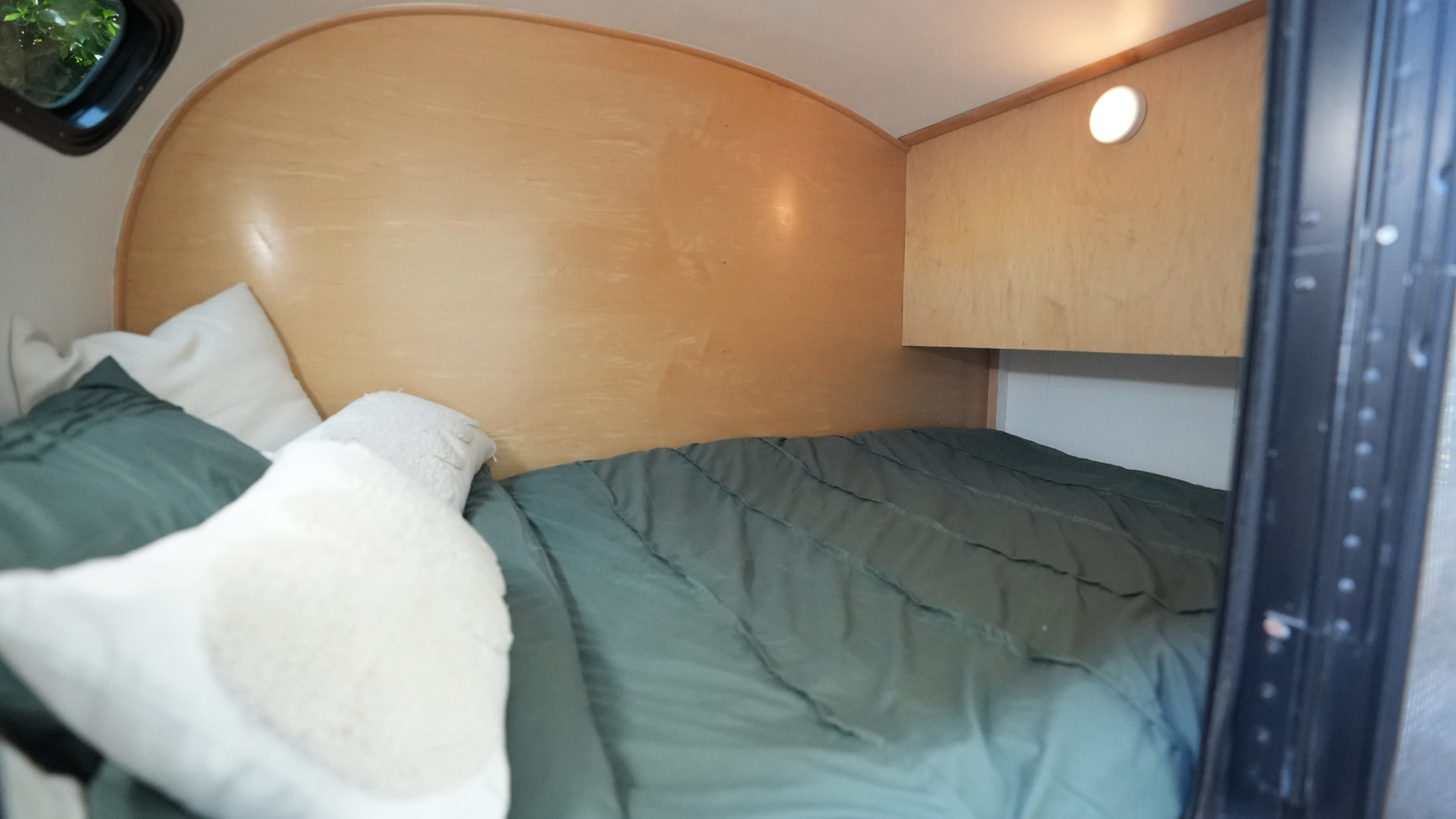 Cozy rv rental bedroom interior featuring wood walls, a bed with a green comforter, white pillows, and a window.. Long Teardrop 2005
