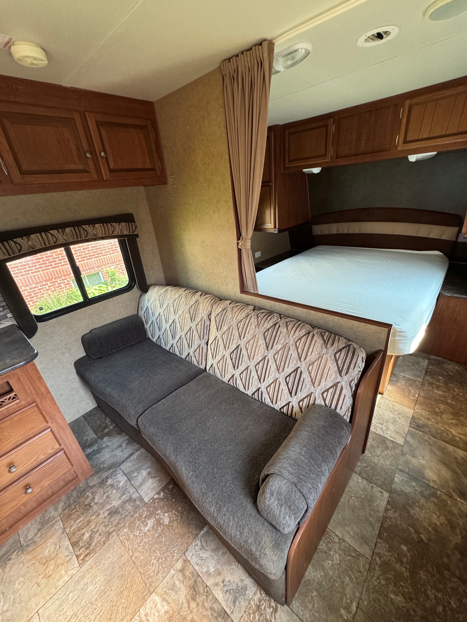 RV rental interior showing a comfortable sofa, a bed with white sheets, and wood cabinetry, with a window view.. Jayco Jay Flight 2013