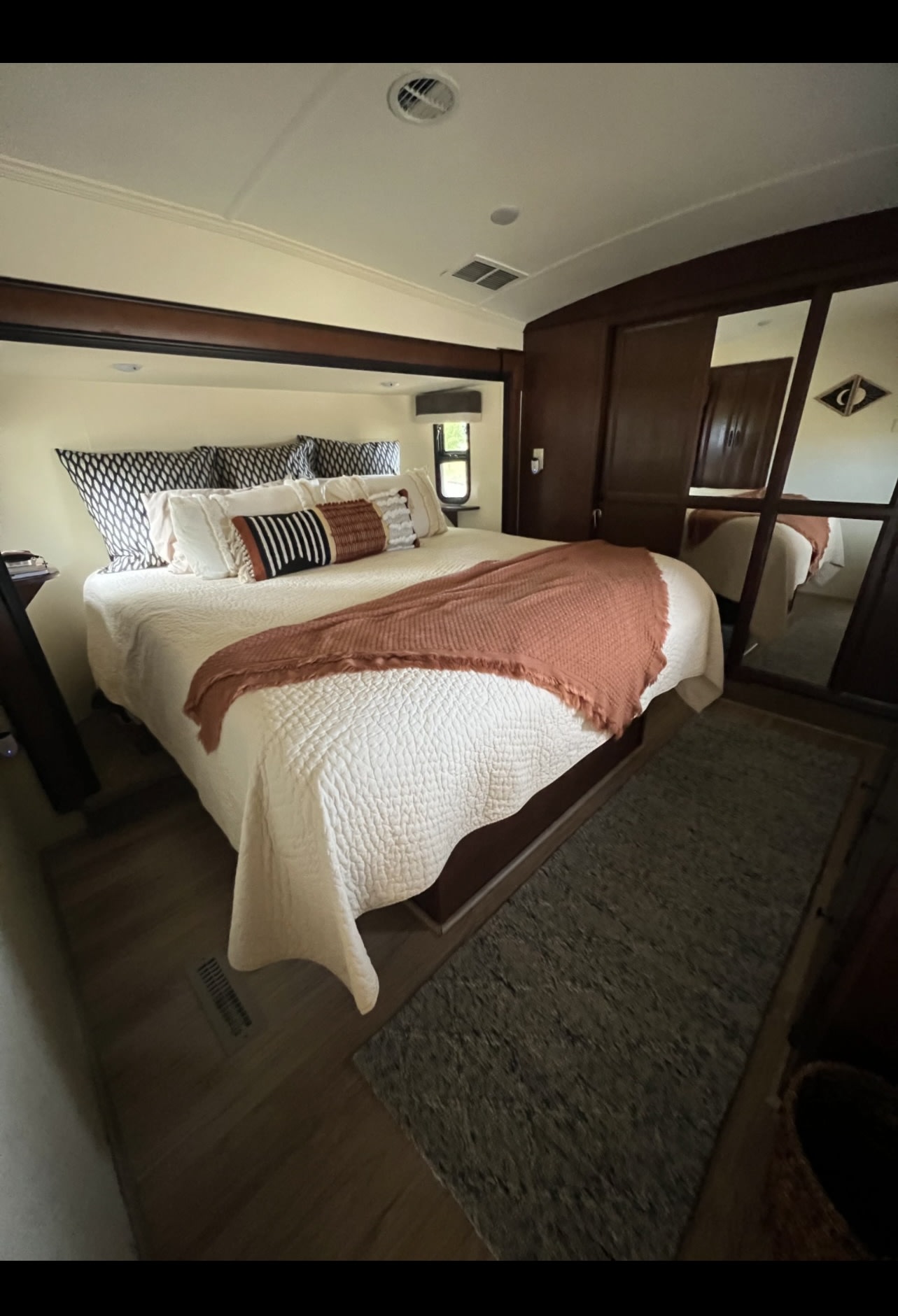 Cozy RV rental bedroom with neutral bedding, a terracotta throw, wood accents, and mirrored closet for a relaxing stay.. Cedar Creek Cedar Creek Fifth Wheel 2014