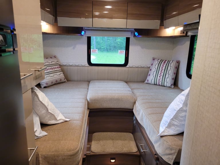 Cozy RV rental interior featuring a U-shaped lounge seating area with cushions and pillows, convertible to a bed.. Winnebago View 2017