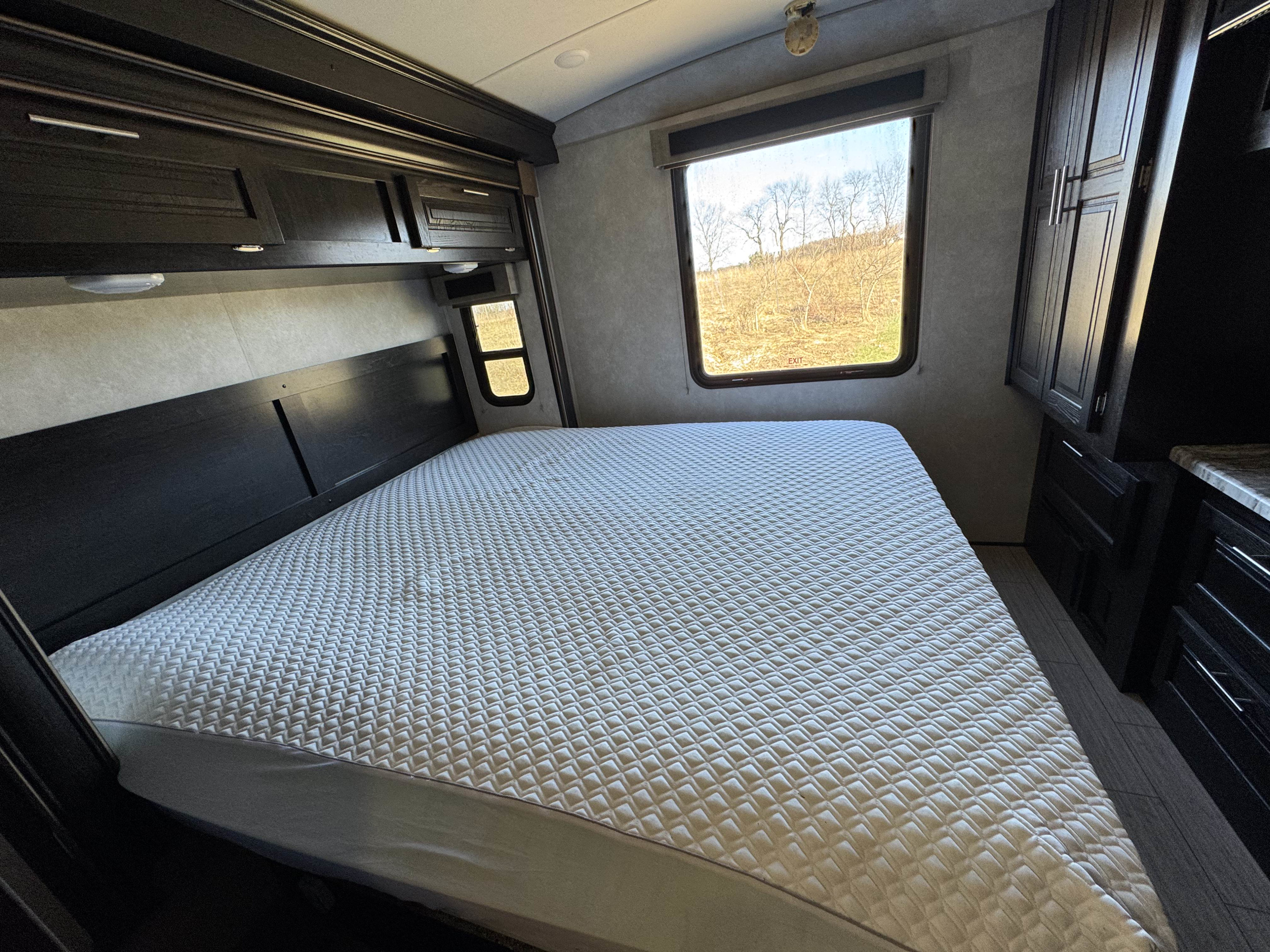 Inside this RV rental, a cozy bedroom features a large bed, dark wood cabinets, and a window with a natural view.. Forest River FR3 30DS 2019
