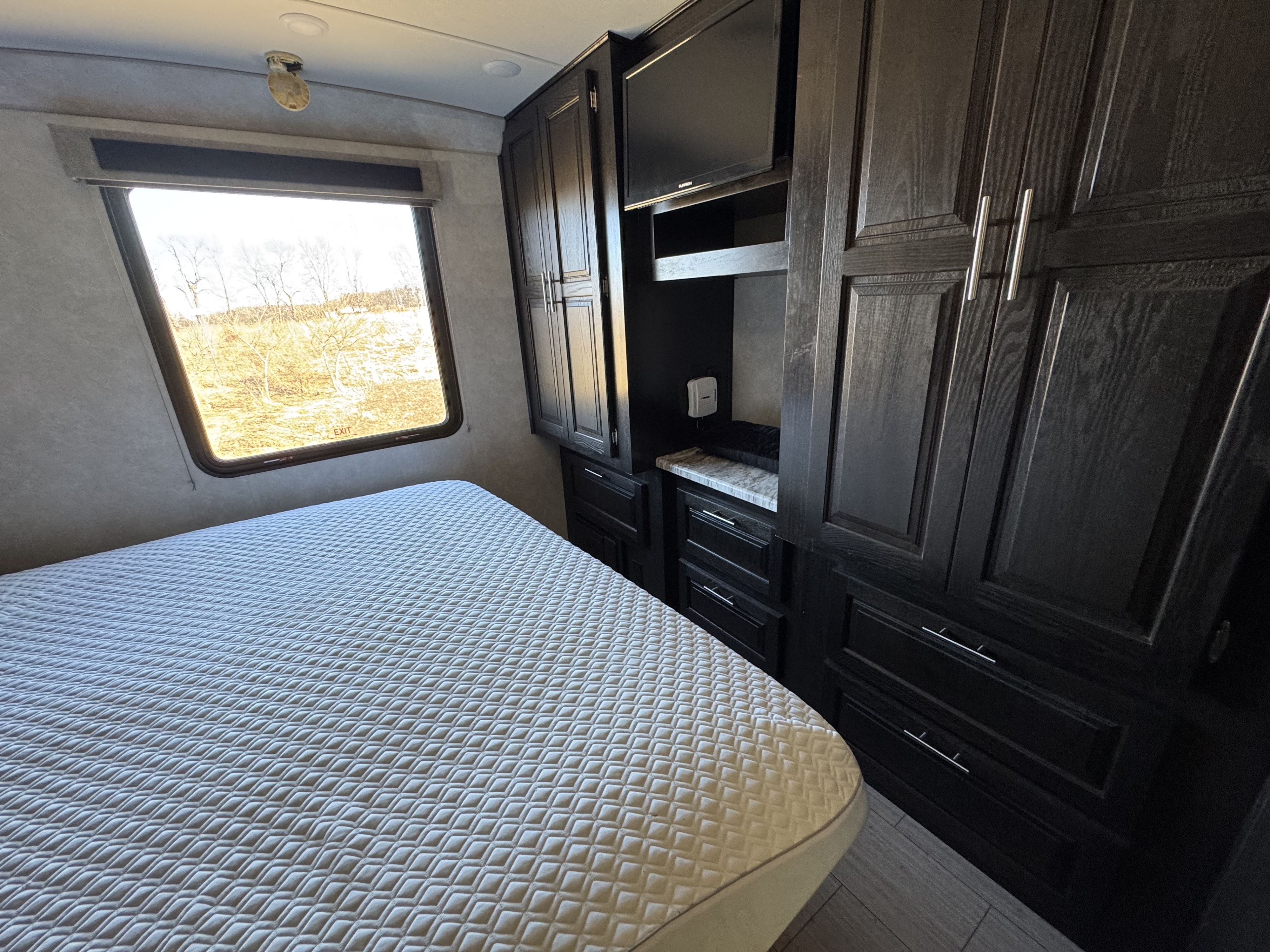 Cozy RV rental bedroom with a comfortable quilted bed, bright window, sleek dark cabinets, and TV setup.. Forest River FR3 30DS 2019