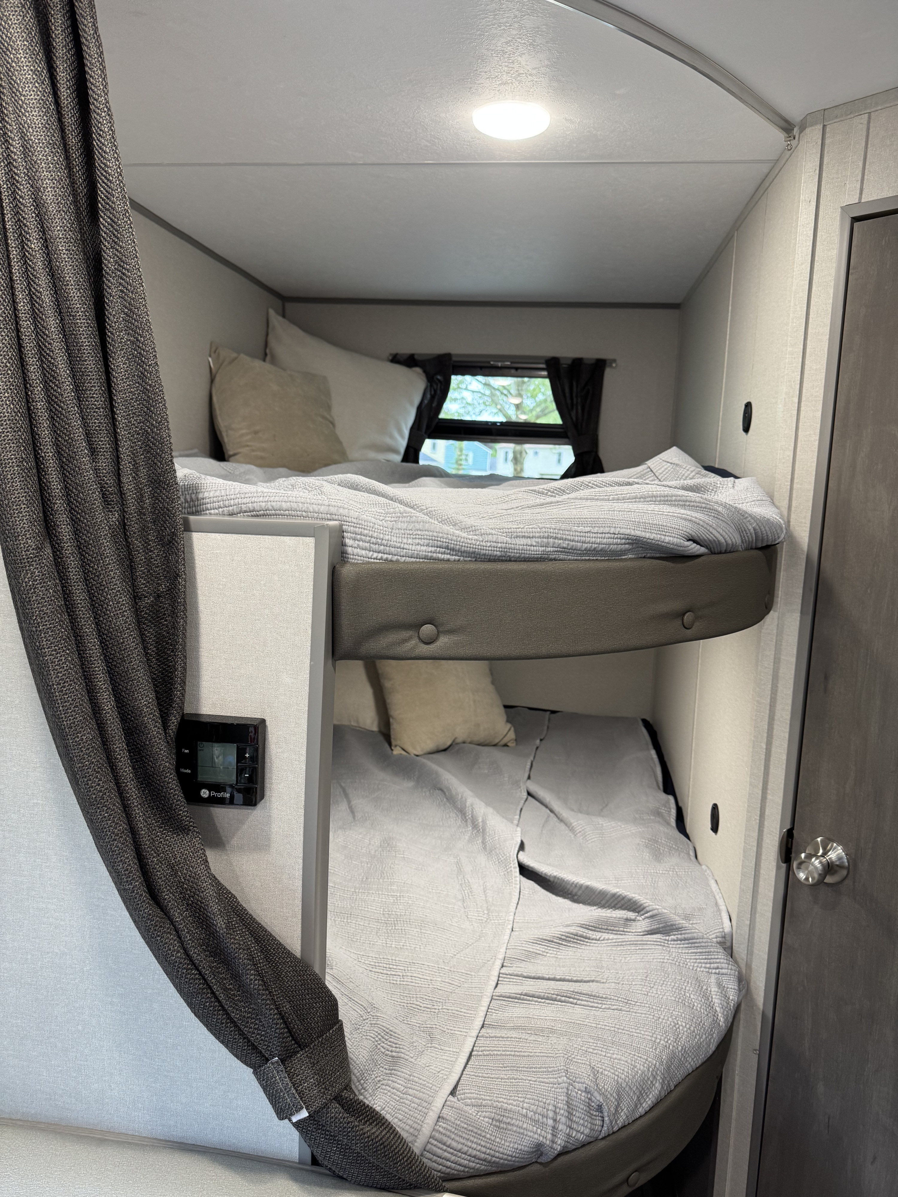 Cozy RV rental bunk beds with light gray bedding, dark window curtains, and a visible GE Profile thermostat on the side wall.. Coachmen Catalina Summit Series 8 2026