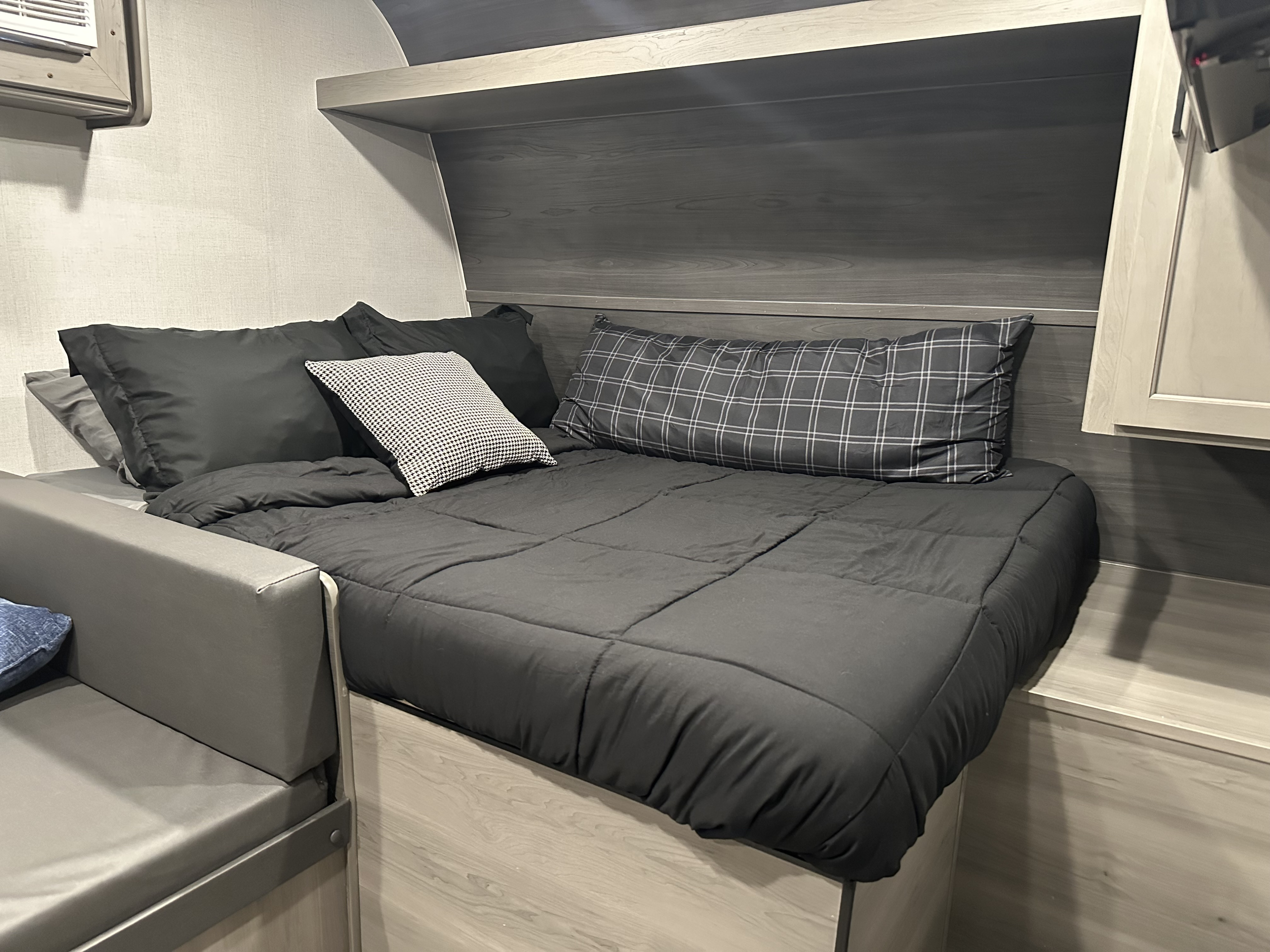Cozy RV rental sleeping area featuring dark bedding, patterned pillows, and a built-in shelf over the bed.. Keystone RV Hideout Sport 2024