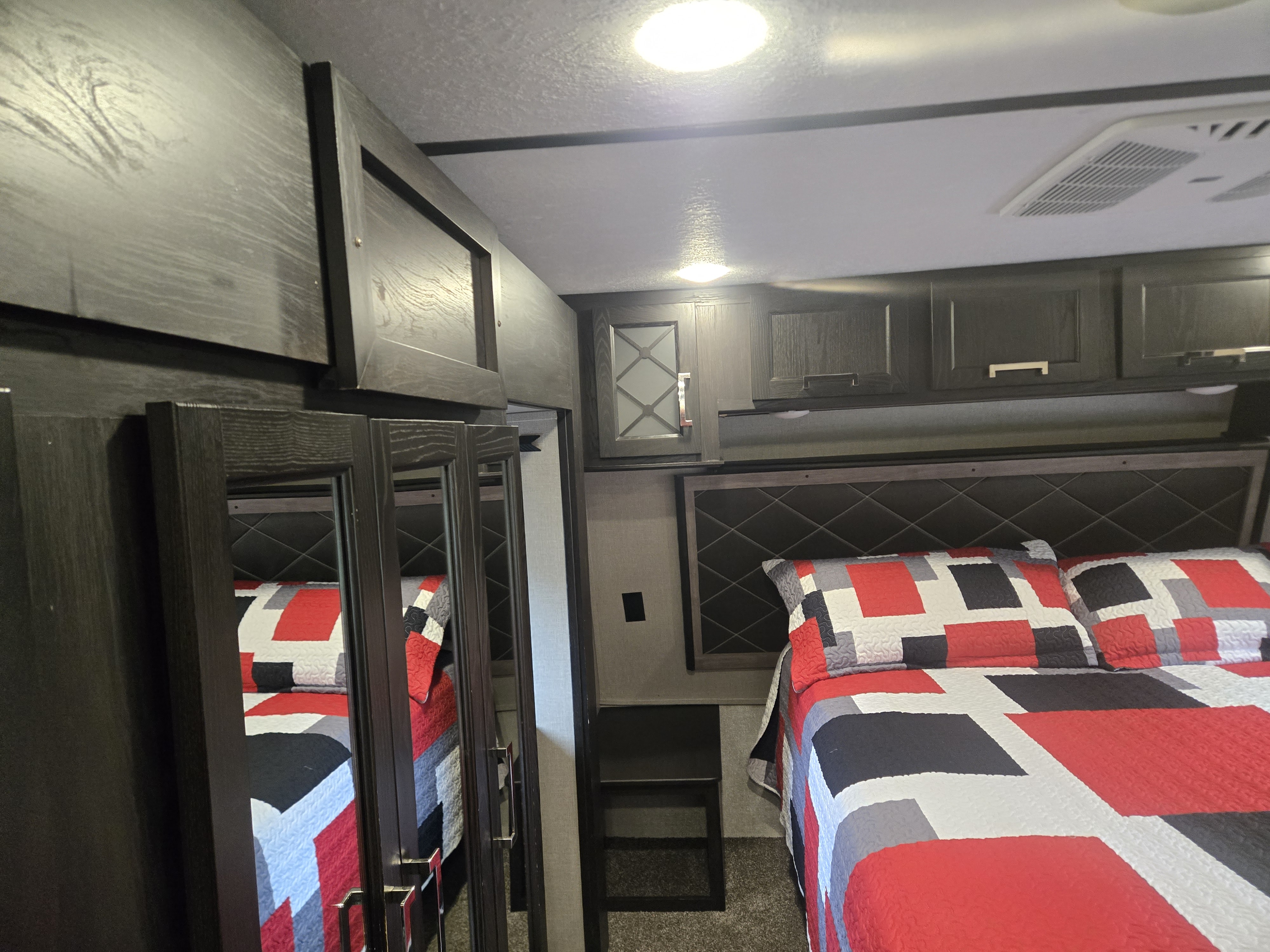 Modern RV rental bedroom with dark cabinets, mirrored closet, and a vibrant red and black patterned bed.. Keystone Fuzion 2018