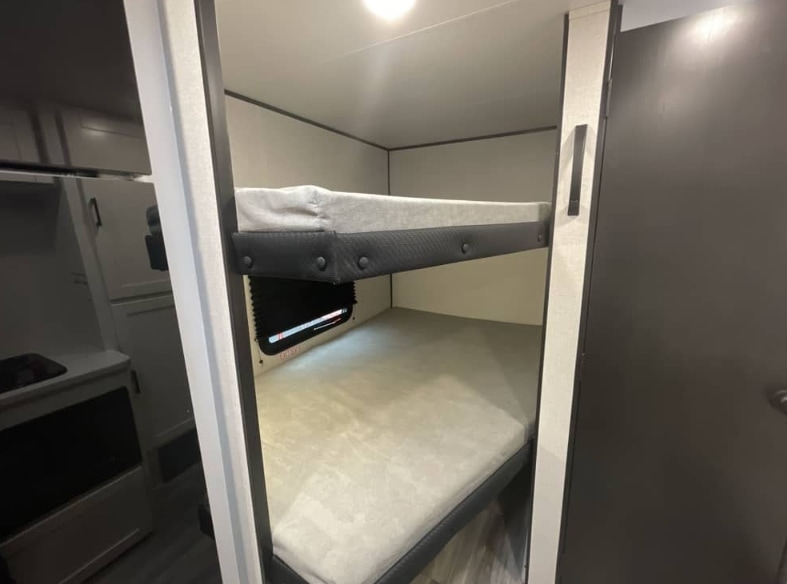 Cozy bunk beds inside this RV rental, perfect for family adventures. The interior also features a glimpse of a kitchen area.. Jayco Jay Flight SLX Sport Edition 2026