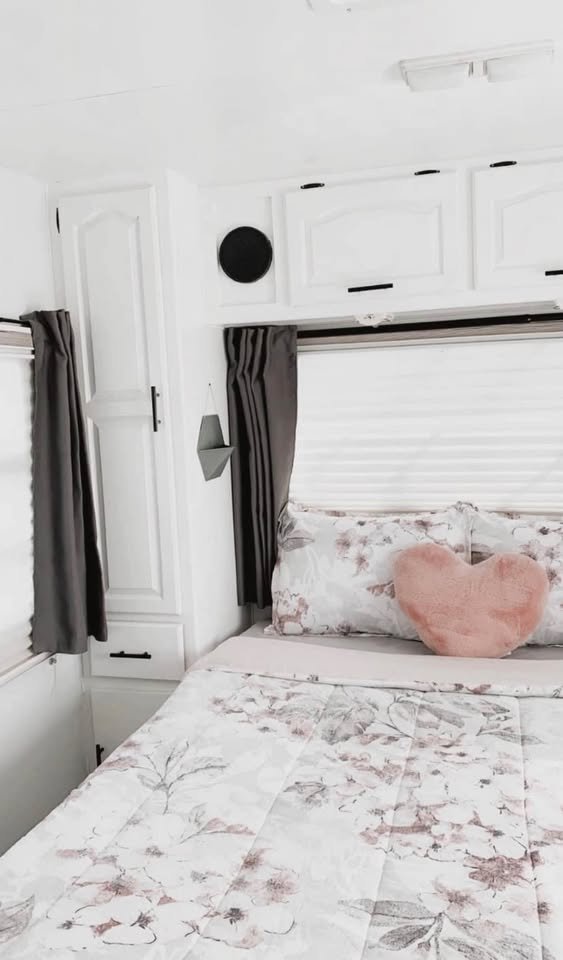 Bright RV rental bedroom features white cabinets, floral bedding, and a cozy pink heart pillow, creating a welcoming interior.. Damon Daybreak 1998