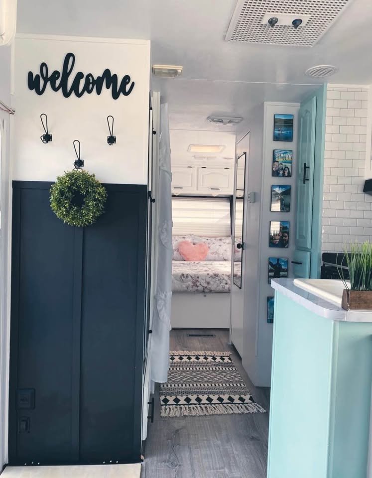 Bright, stylish RV rental interior: 'Welcome' sign, dark blue paneling, patterned rug, light blue kitchen, cozy bed ahead.. Damon Daybreak 1998