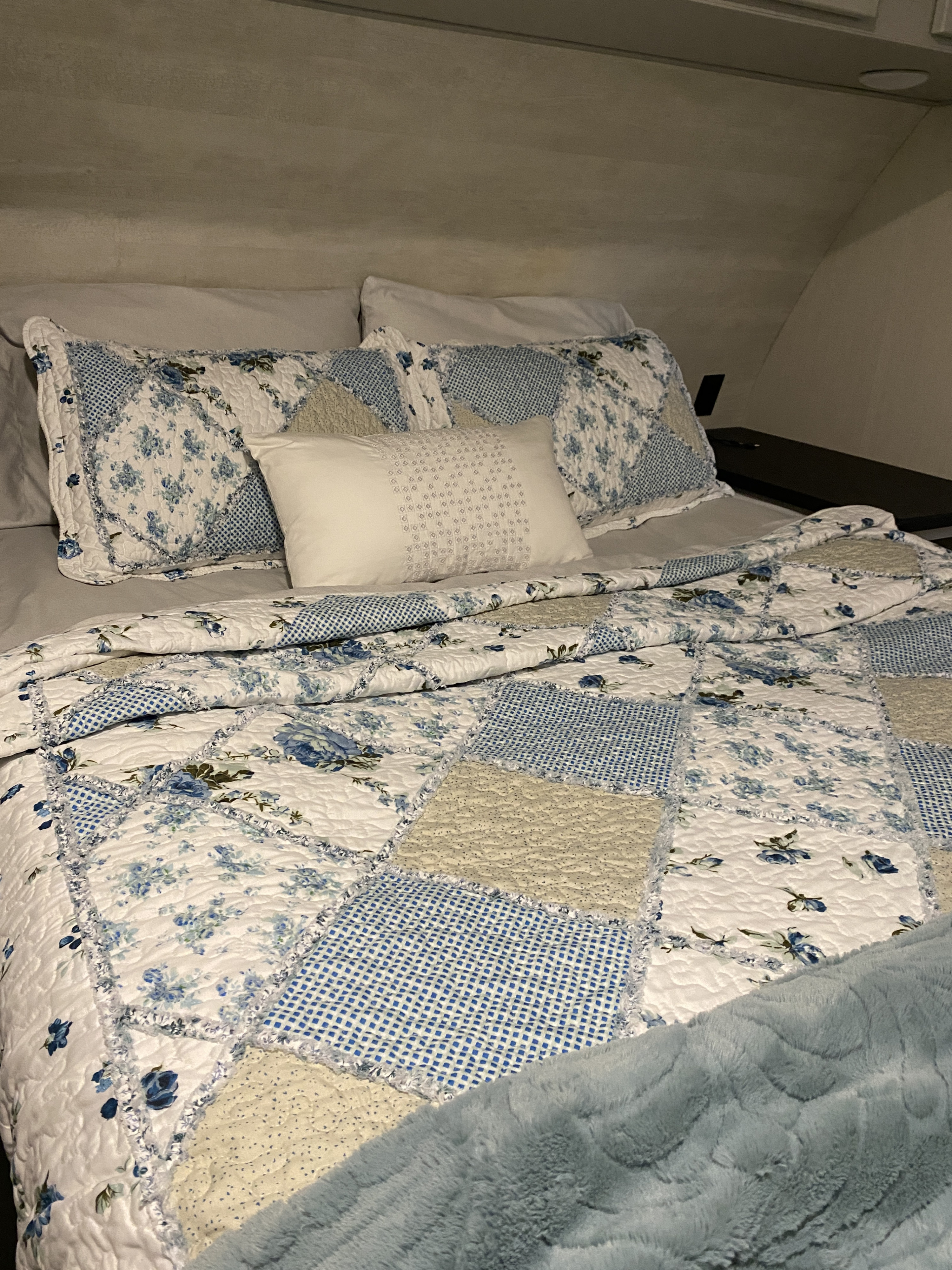 Cozy RV rental bedroom featuring a bed with a blue and white floral patchwork quilt and a soft blue blanket.. Forest River Vibe 2021